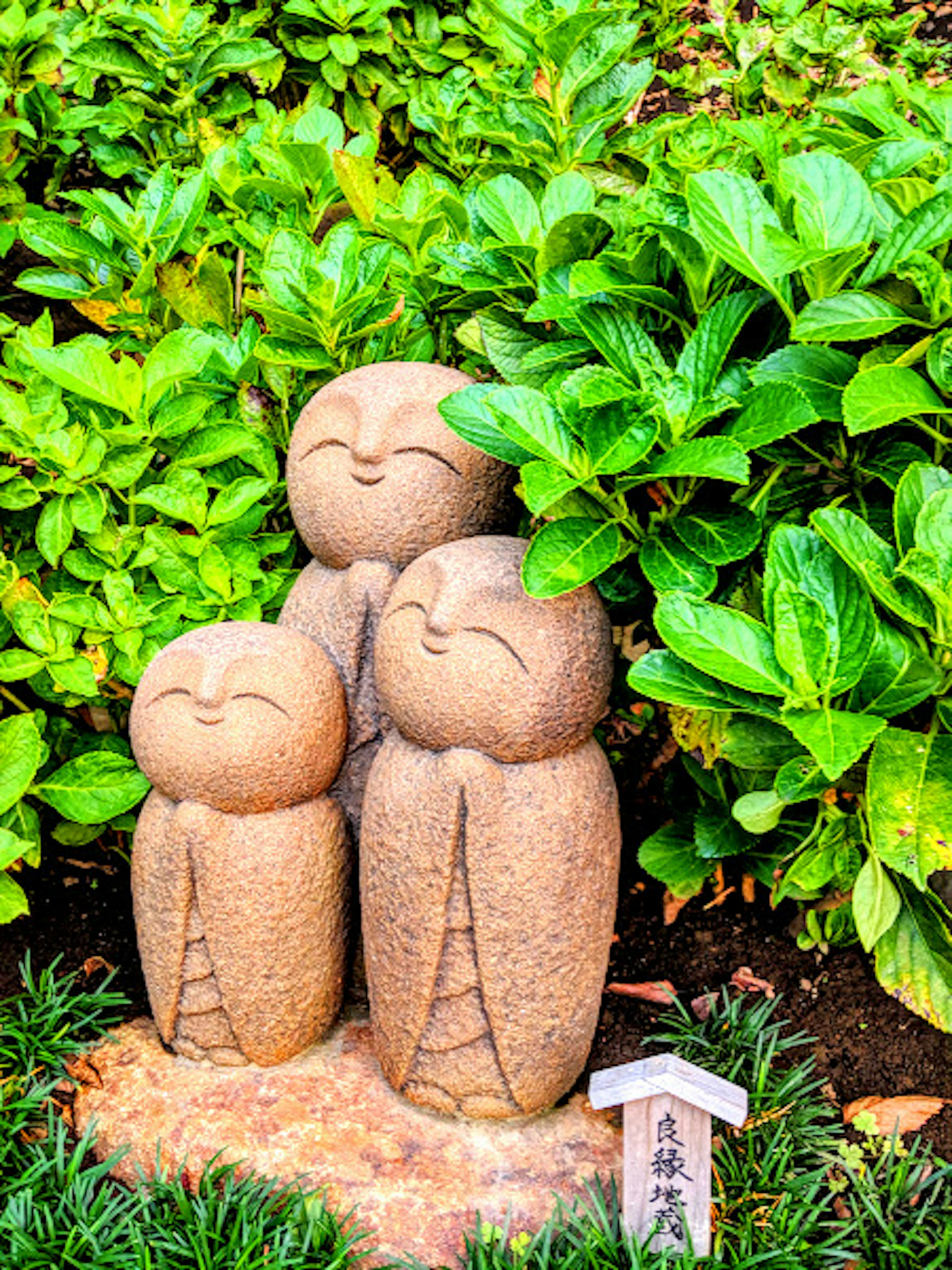 Drei niedliche Steinskulpturen in einem Garten umgeben von üppigem grünem Pflanzen mit lächelnden Gesichtern