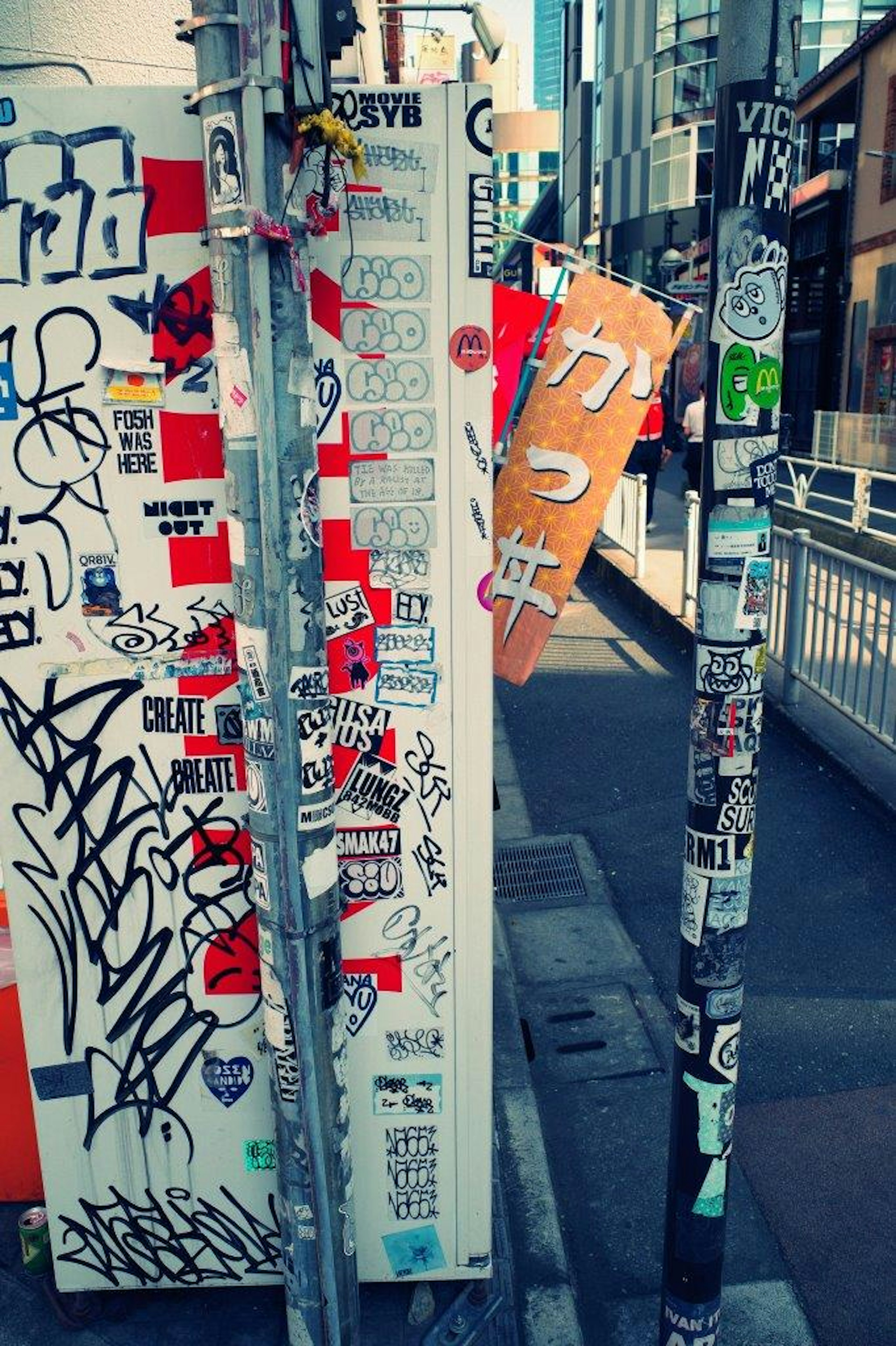 Image of a street pole and sign covered in stickers and graffiti