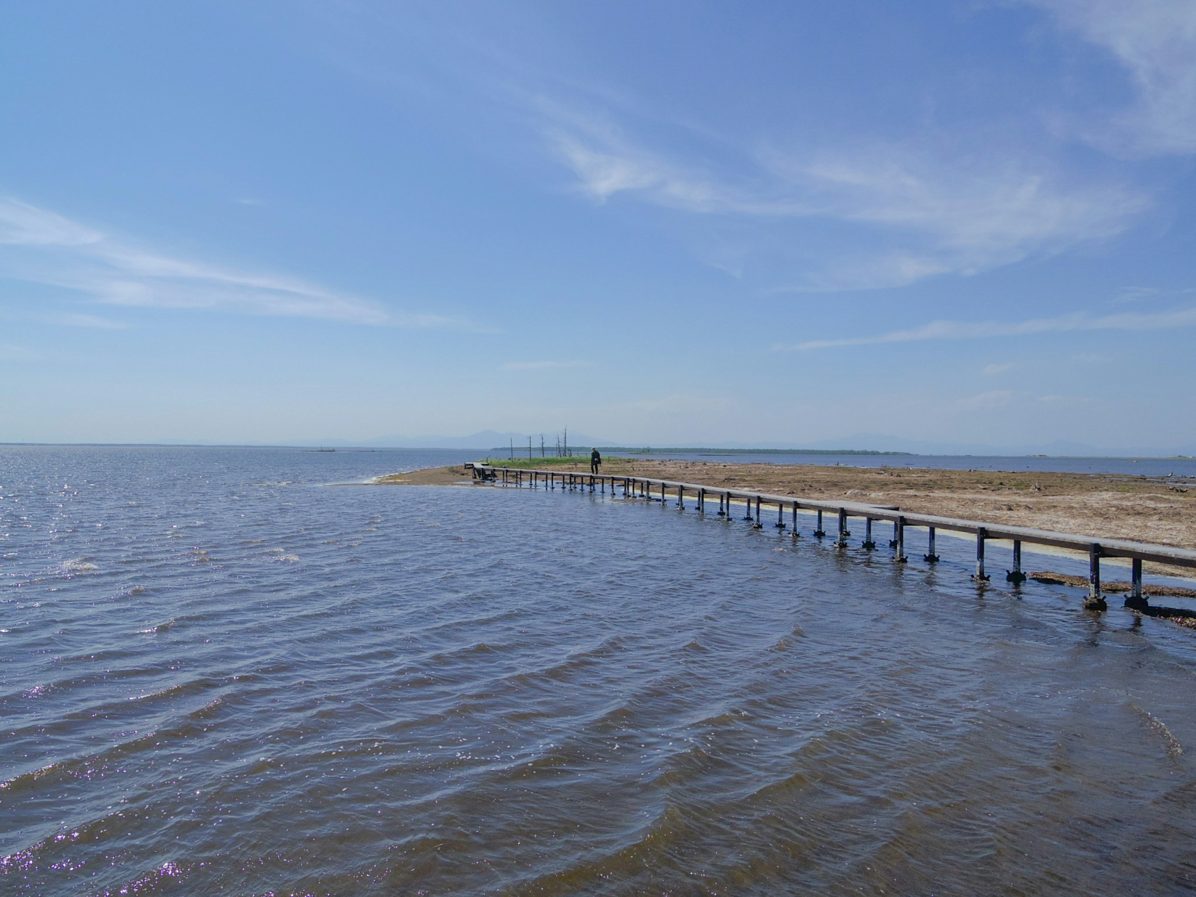 Muelle de madera que se extiende sobre aguas tranquilas bajo un cielo azul claro