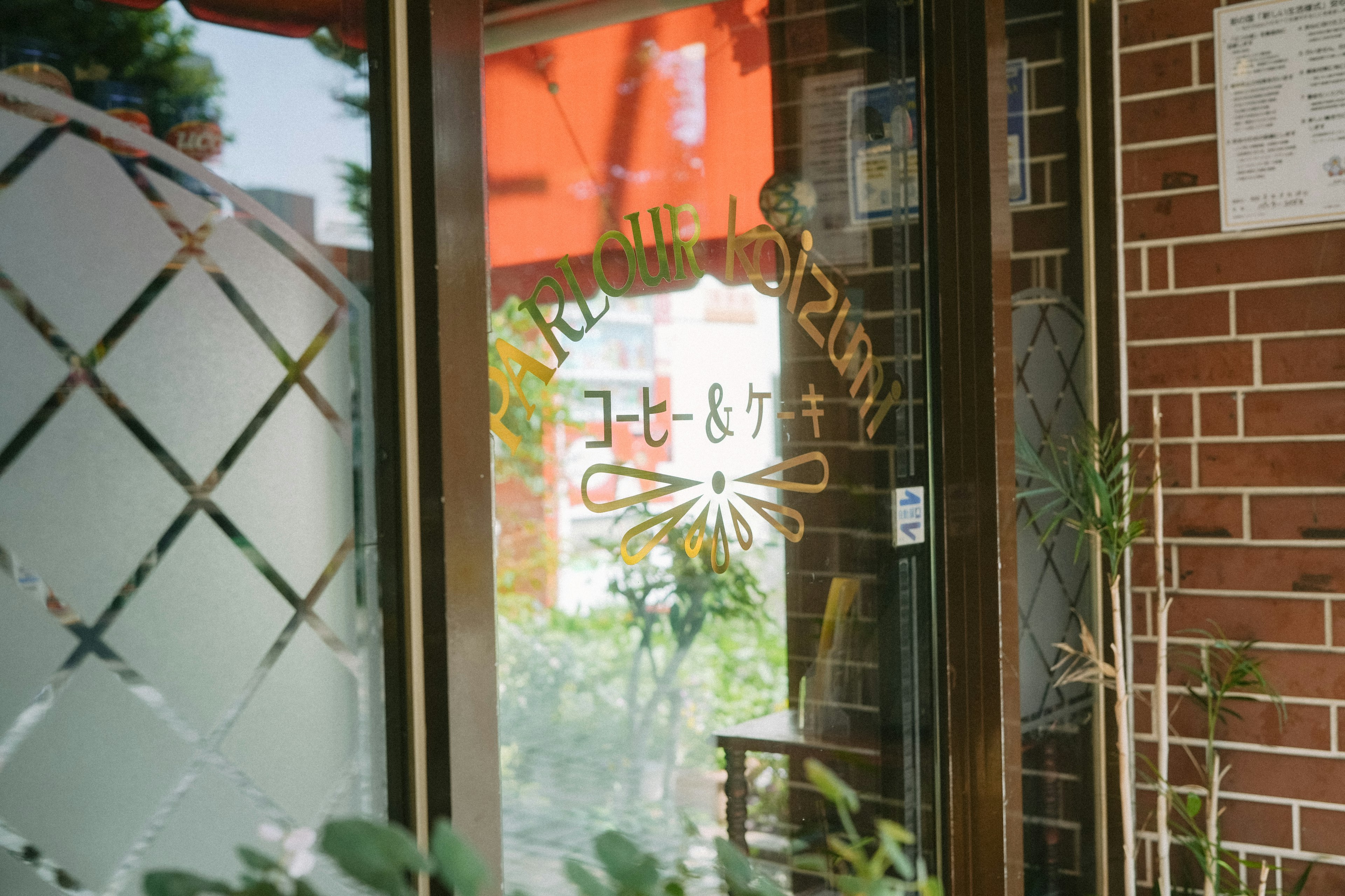 赤い屋根の下にあるカフェの入口 窓に描かれたロゴと植物が見える