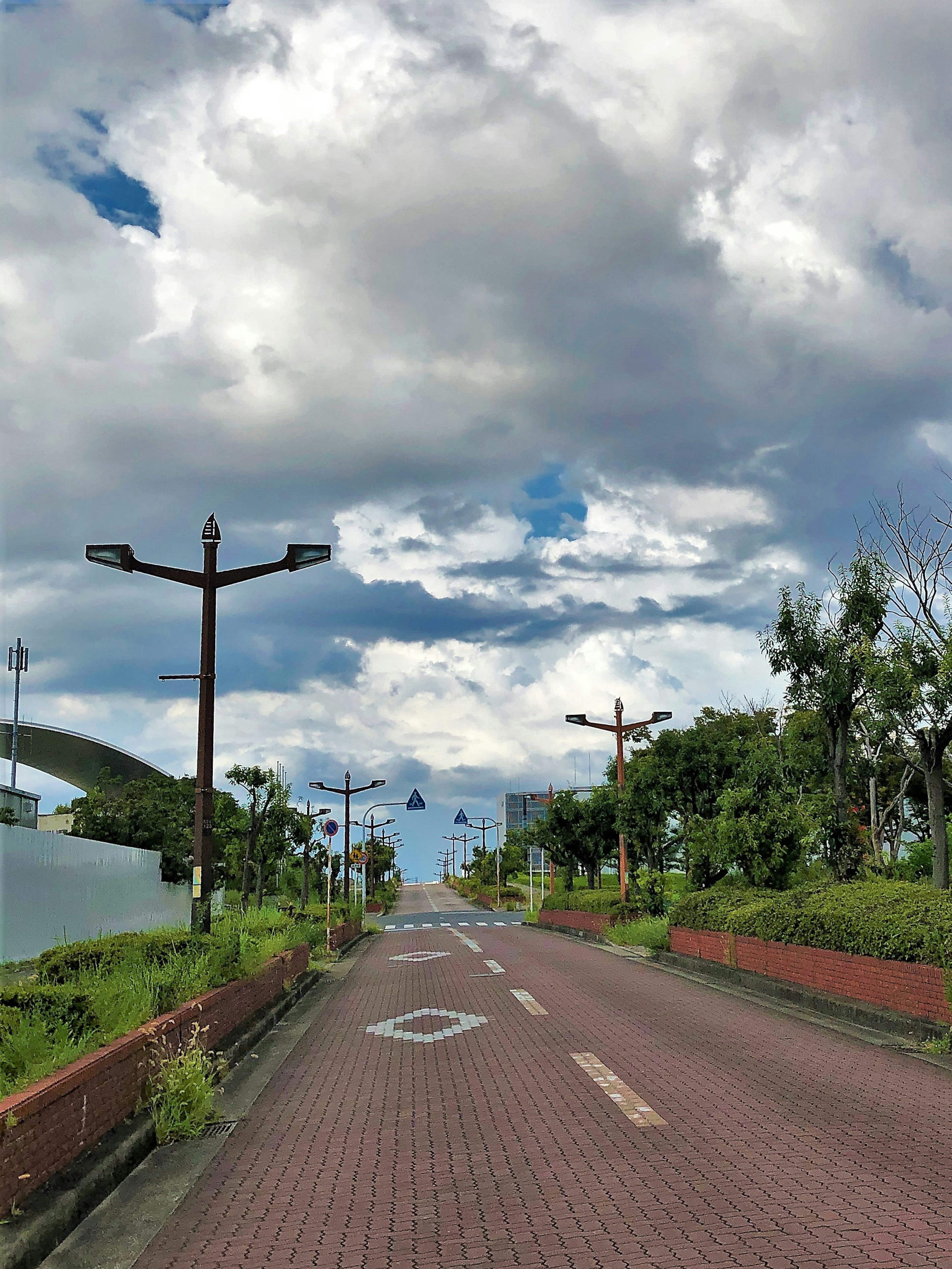 Una carretera tranquila rodeada de cielos azules y nubes con pocas farolas y señales de tráfico