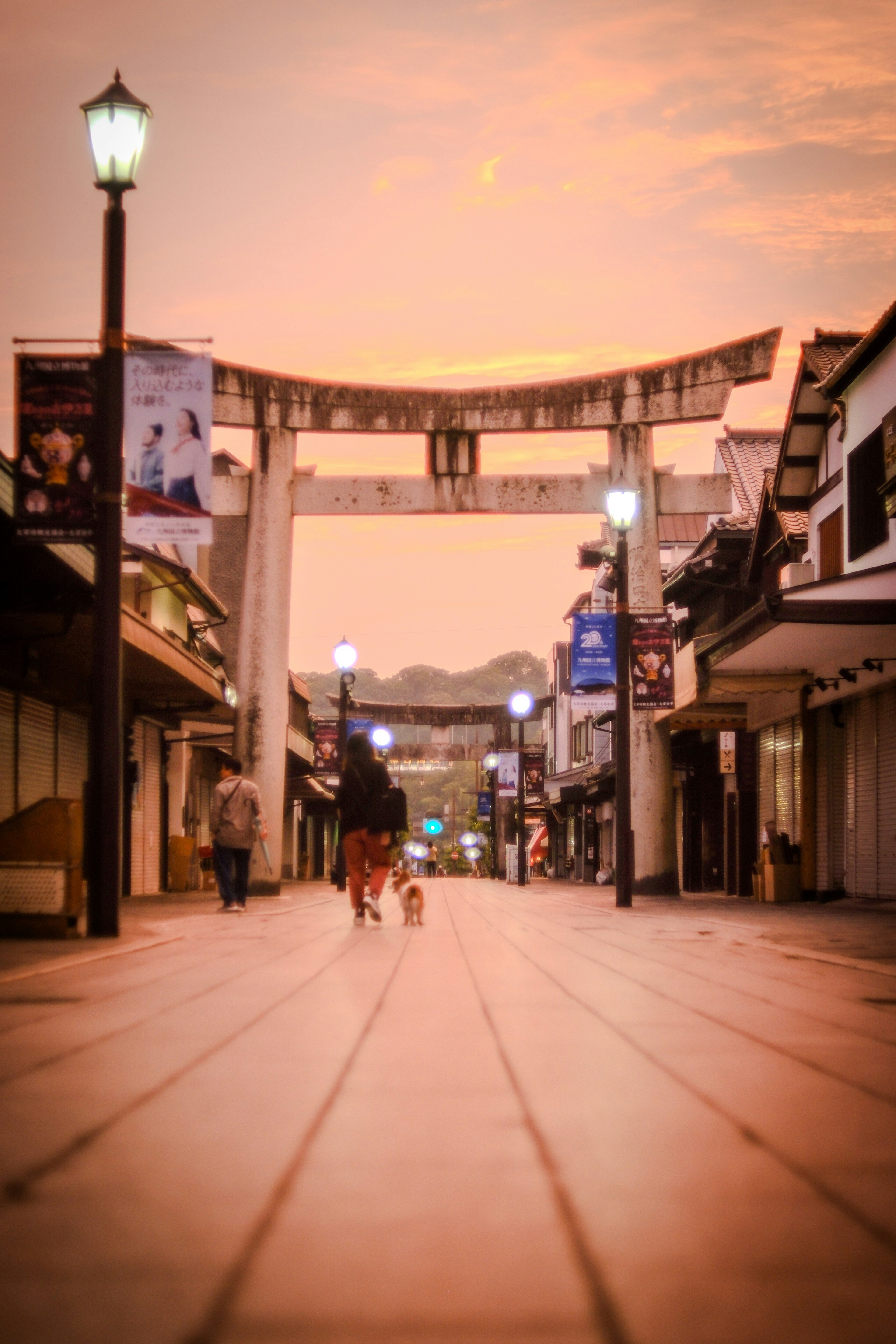A person walking a dog under a torii gate at sunset