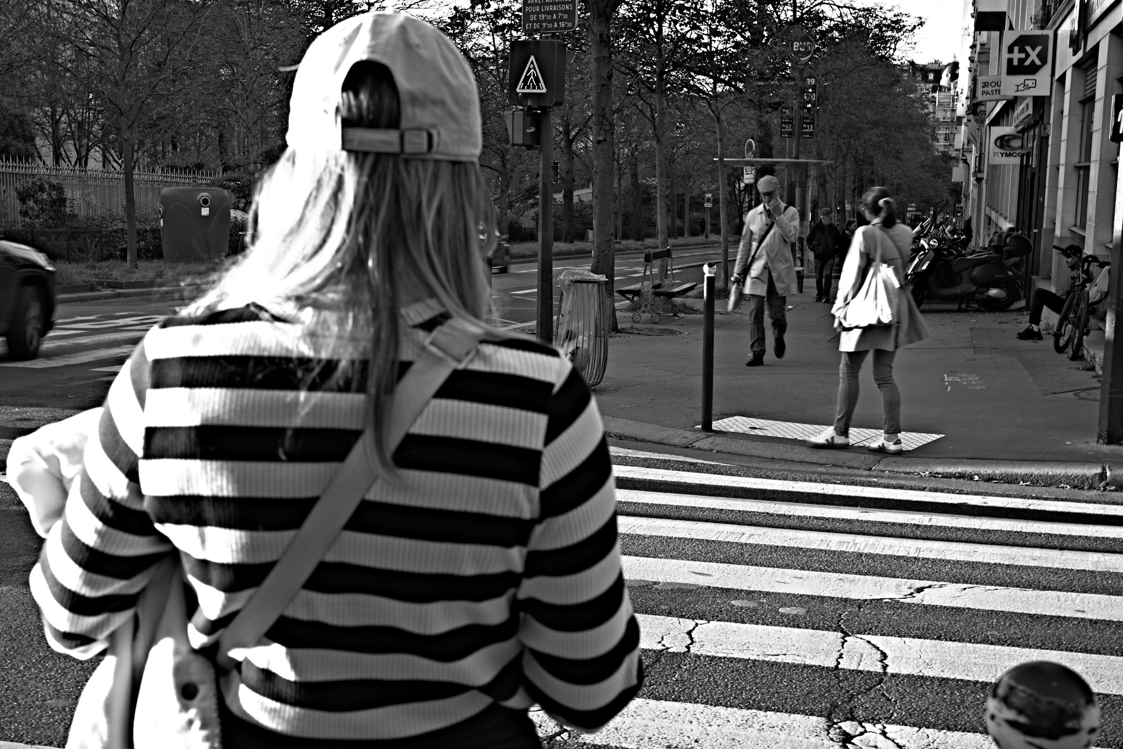 A woman in a striped shirt observes another woman in white clothing at a crosswalk