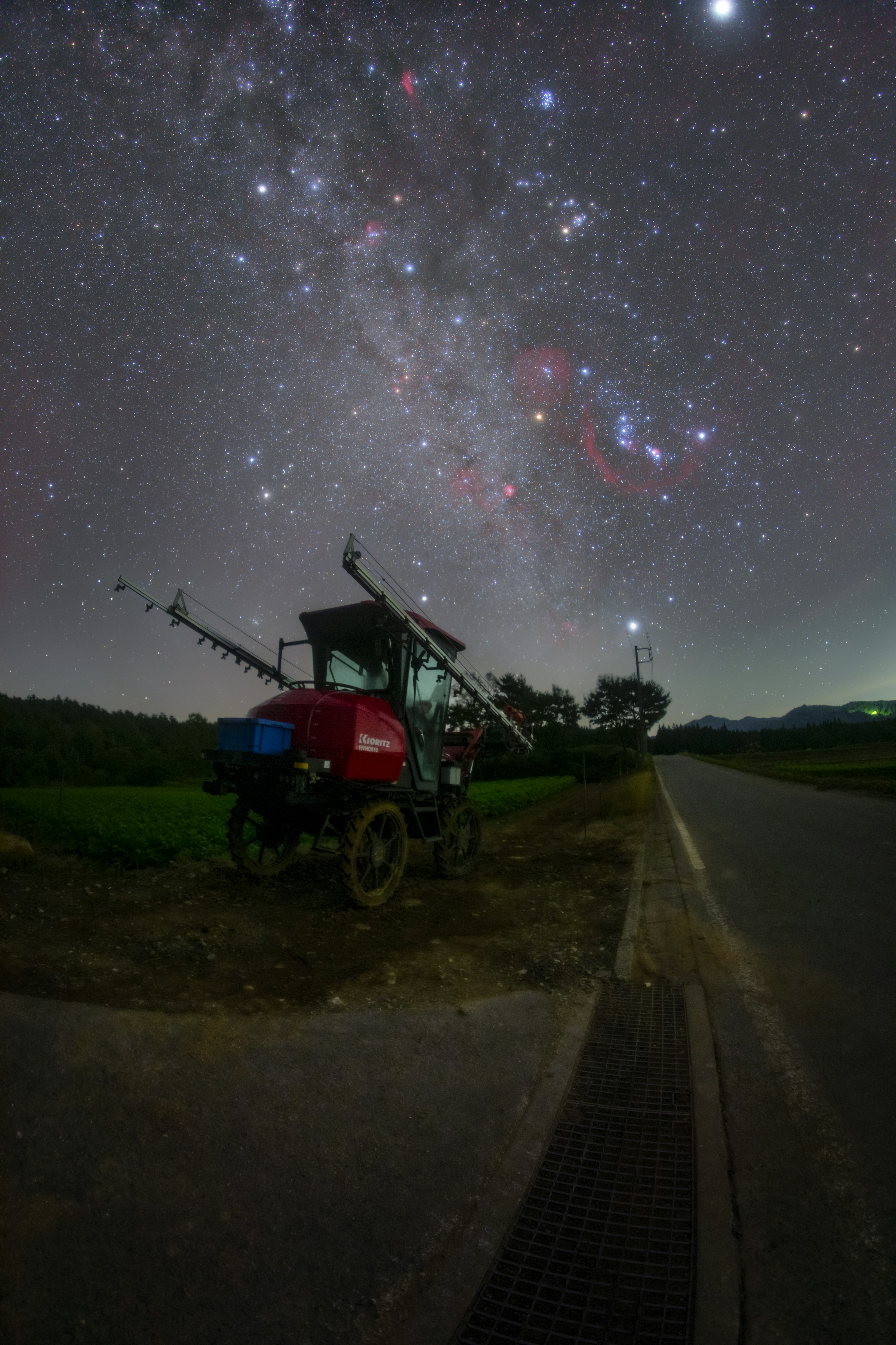 星空の下にある赤いトラクターと農道の風景