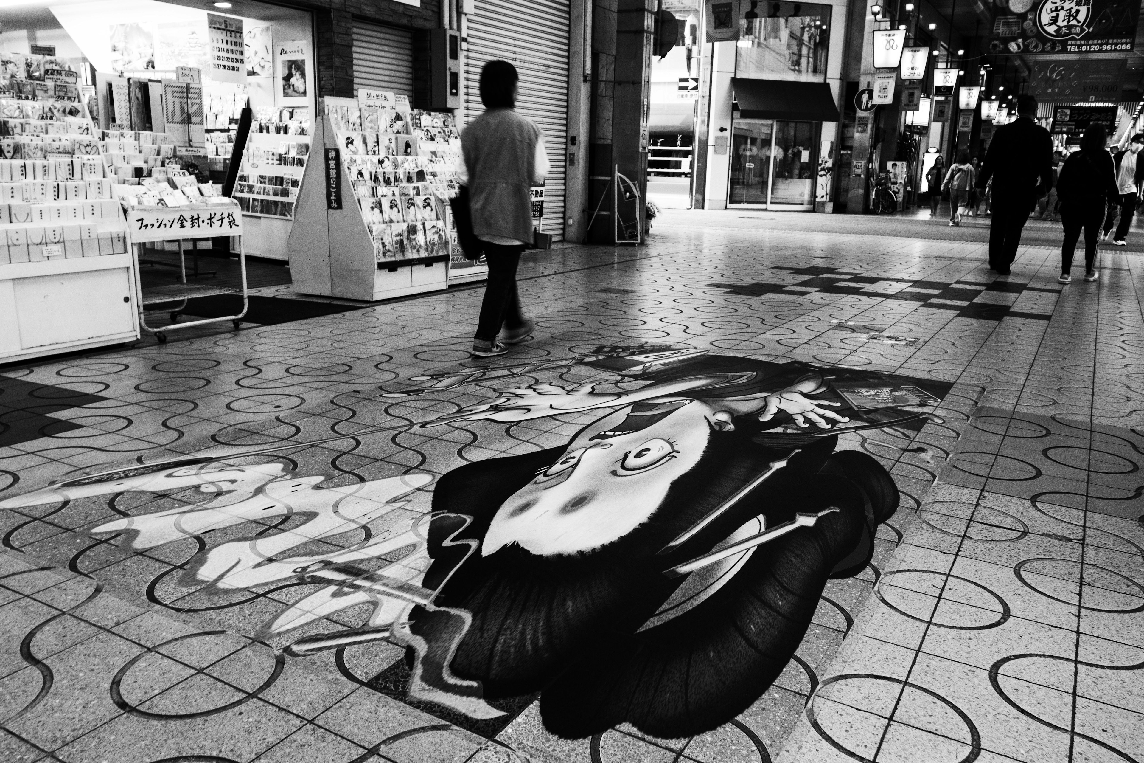 Une personne marchant sur une fresque d'art de rue en noir et blanc au sol