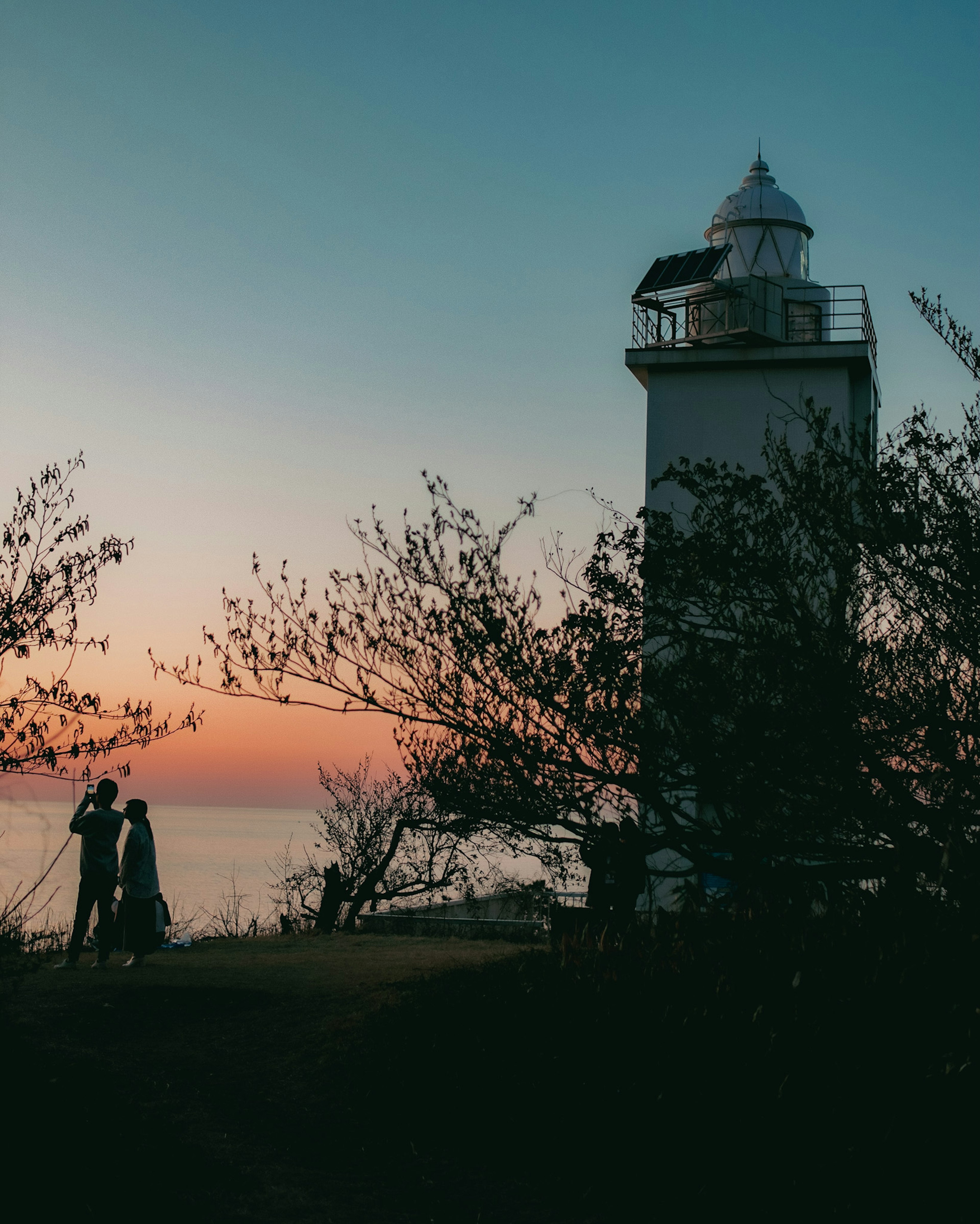 Silhouette eines Paares neben einem Leuchtturm bei Sonnenuntergang am Meer