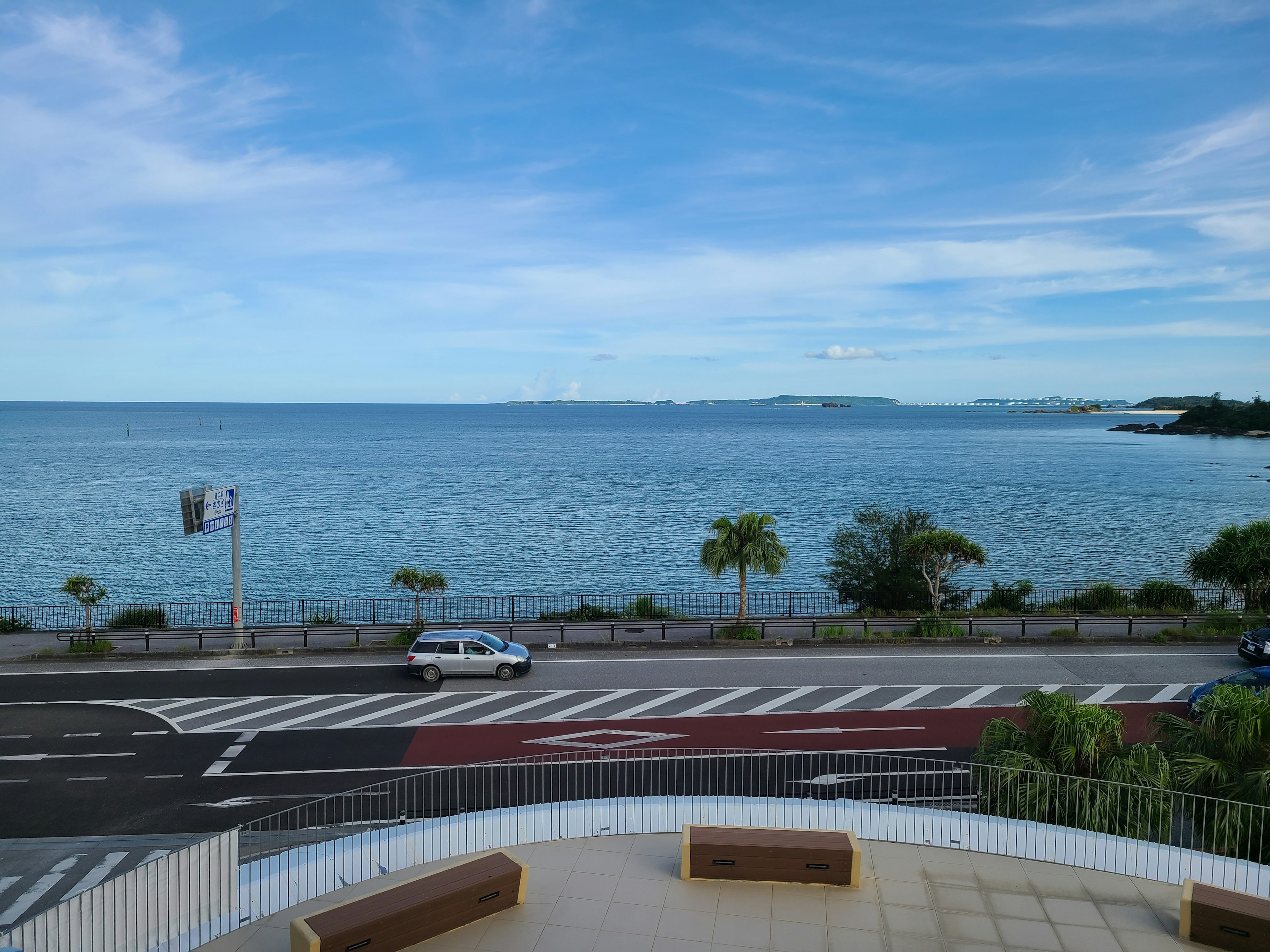 Pemandangan indah laut biru dan langit dengan jalan yang memiliki mobil dan pohon palem