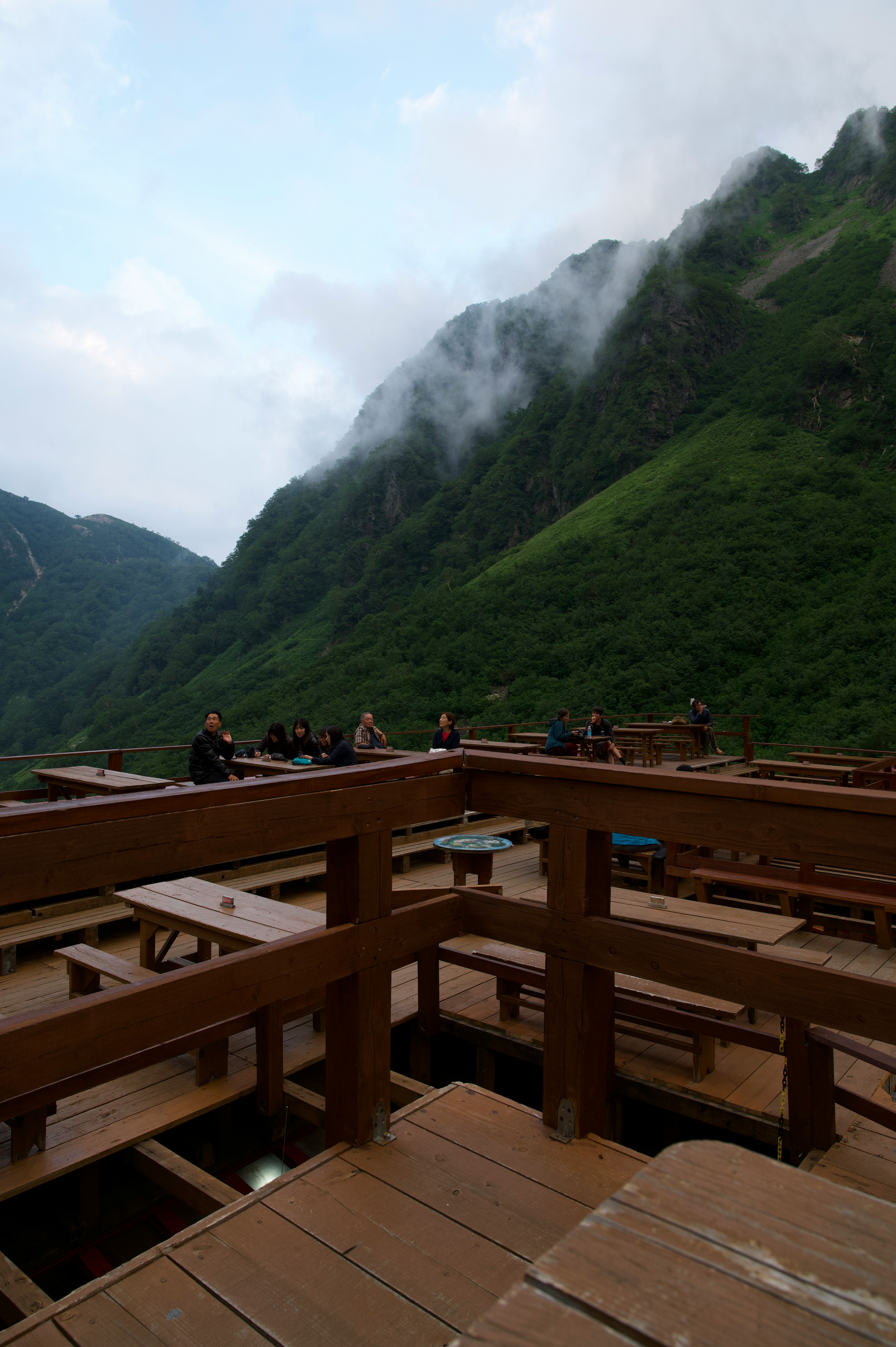 木製露台上人們聚集，四周環繞著山脈和霧氣