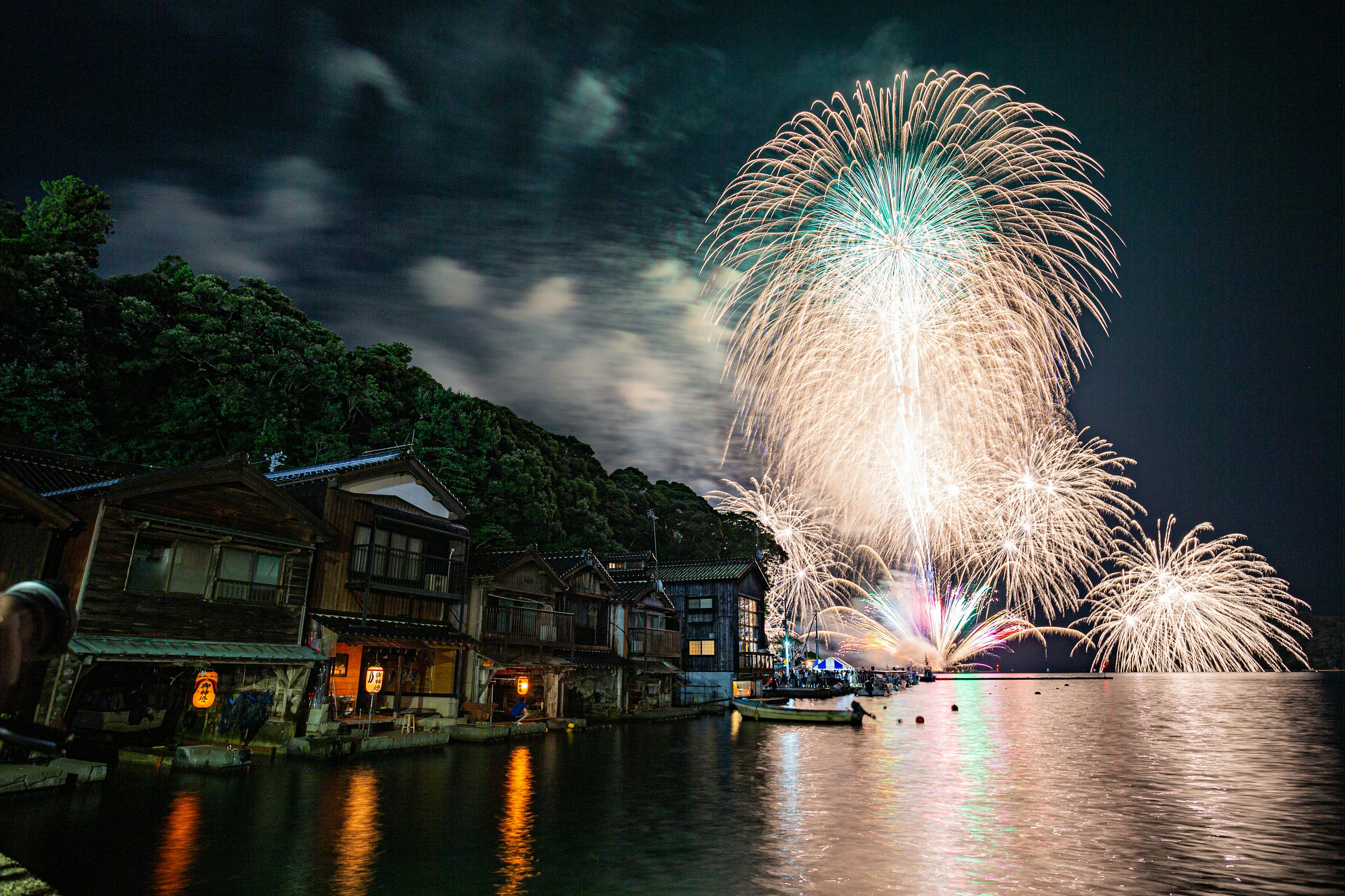 Des feux d'artifice illuminent le ciel nocturne au-dessus de maisons traditionnelles au bord de l'eau