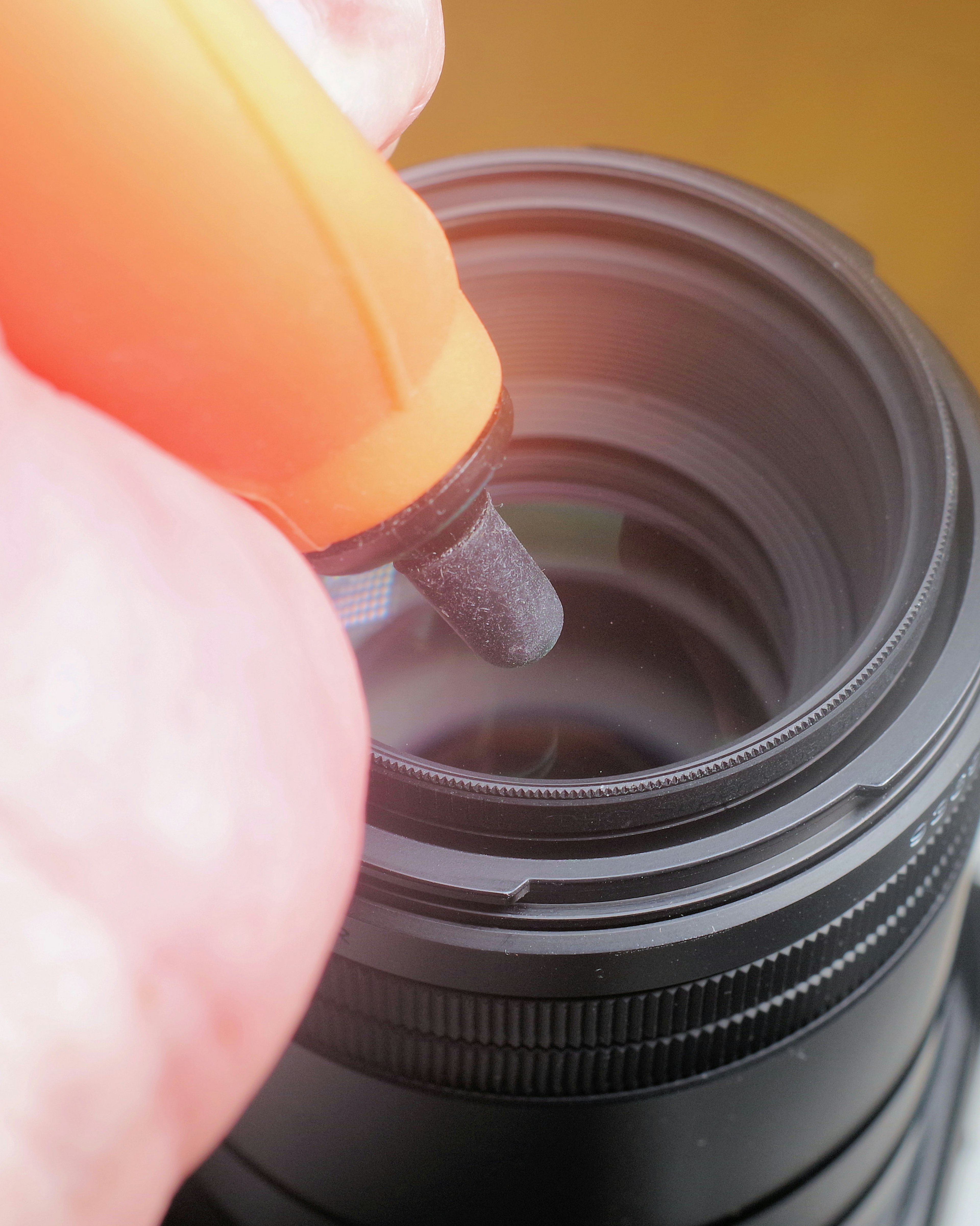 Hand using an orange pen to clean the inside of a camera lens