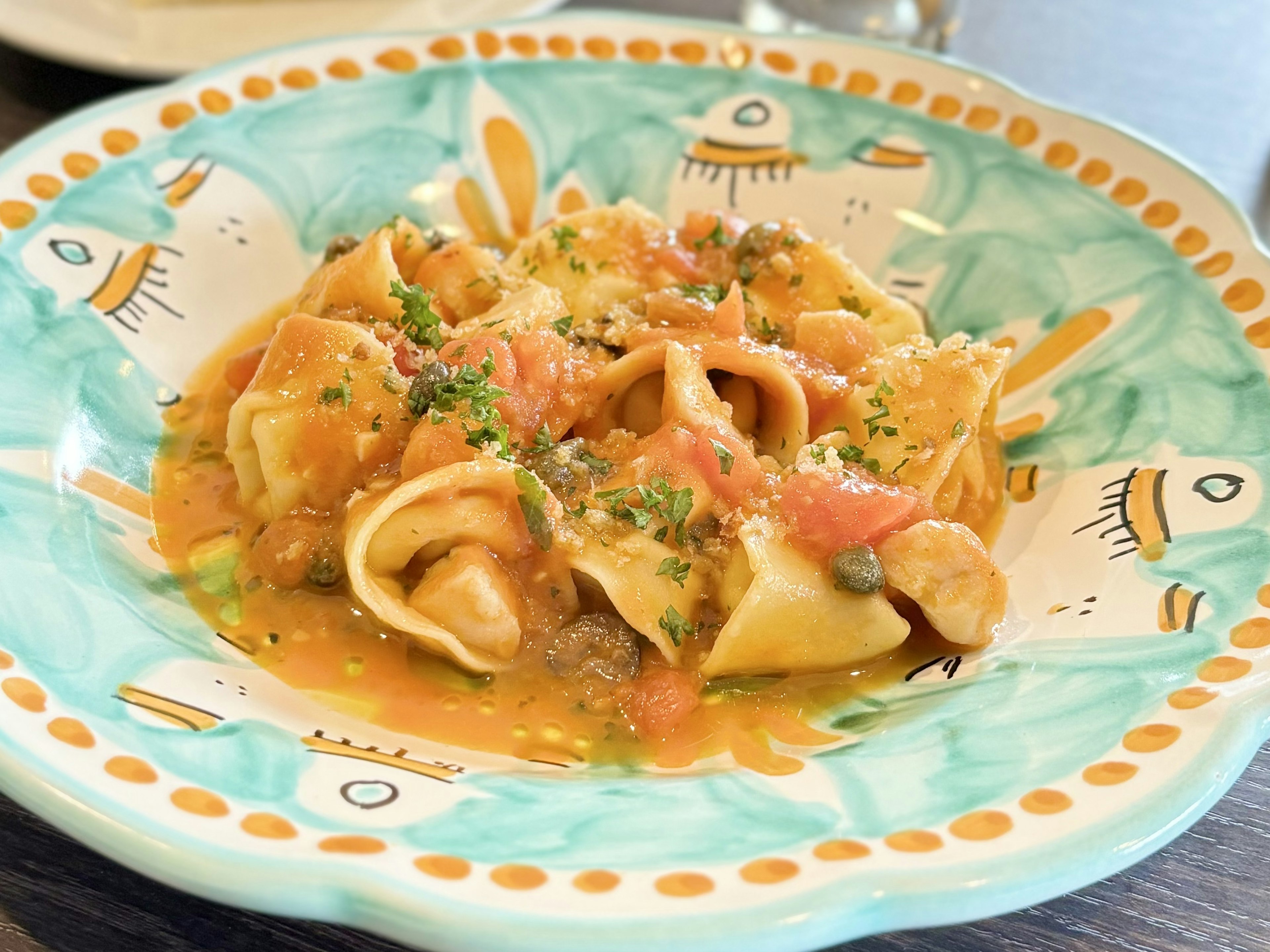 Pastagericht auf einem blauen Dekoteller serviert mit Tomatensauce und Kräutern