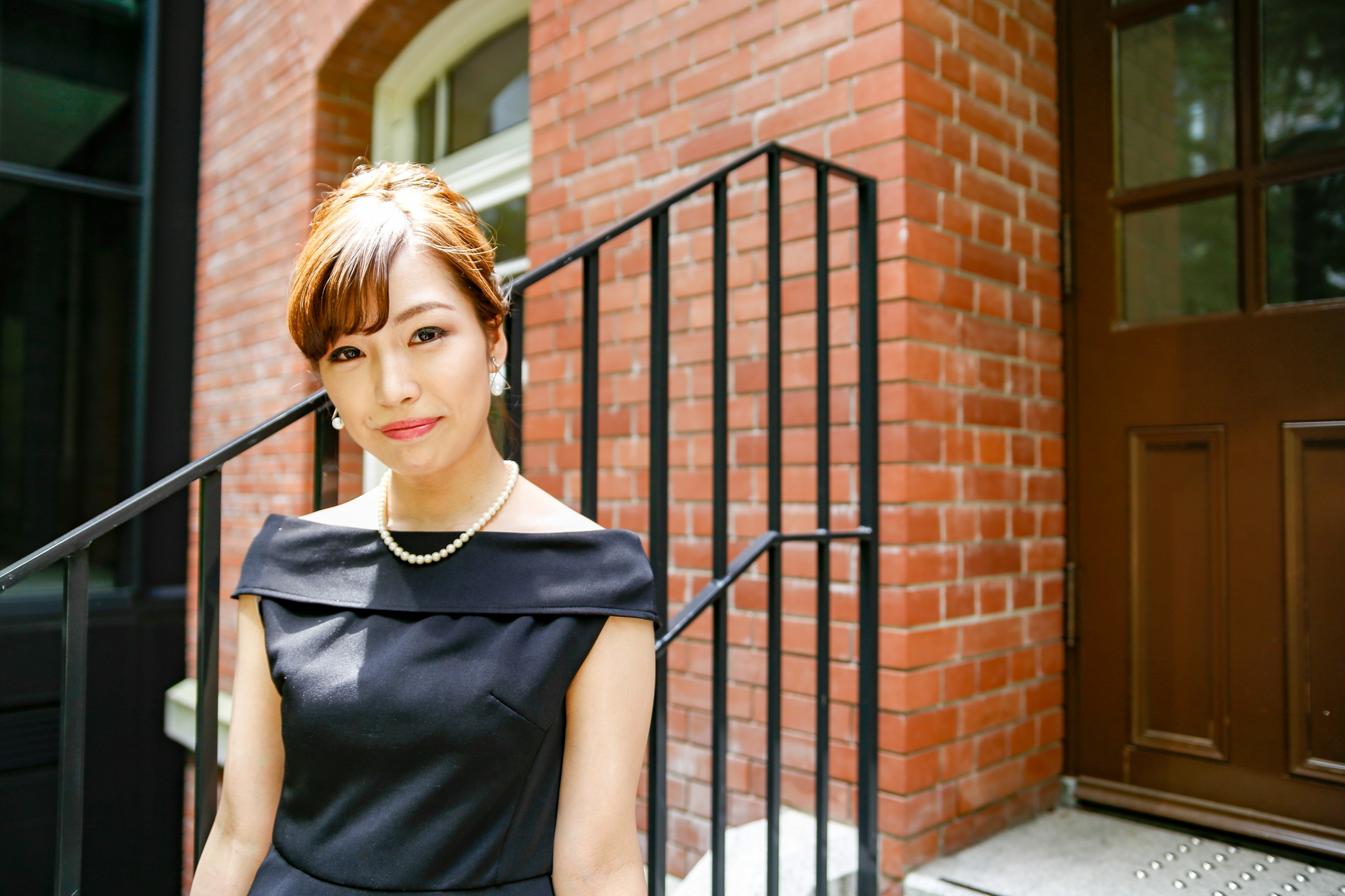 A woman in a black dress stands in front of a brick wall