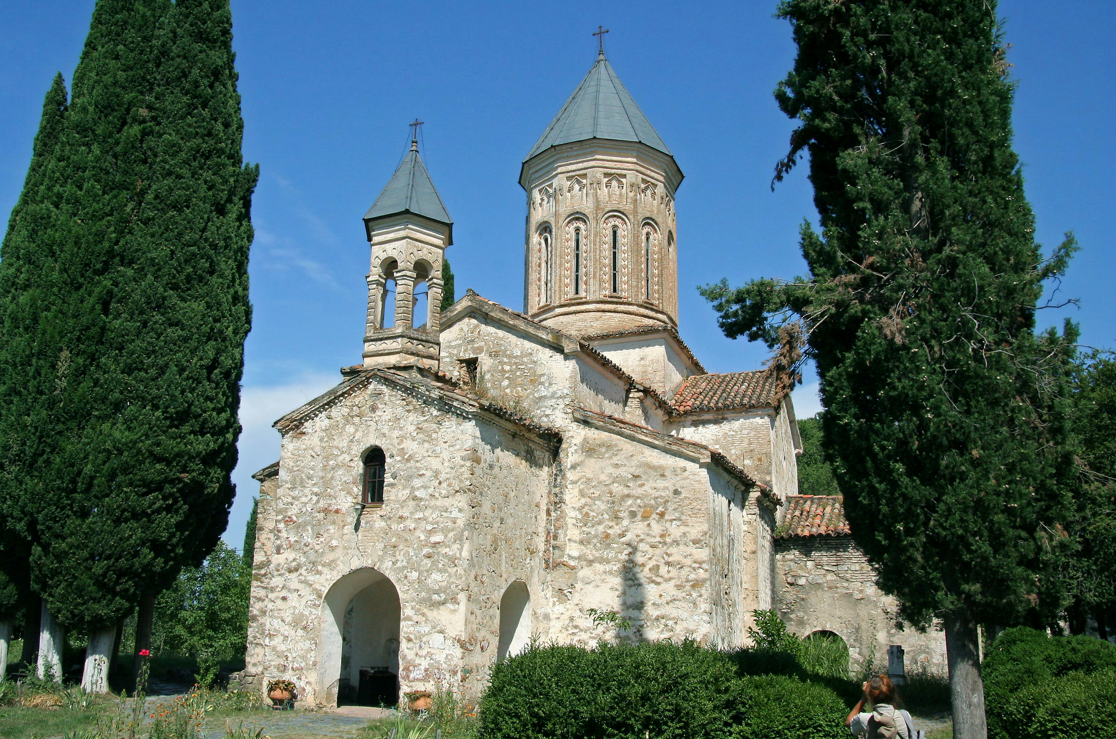 Chiesa in pietra con alberi alti sotto un cielo blu