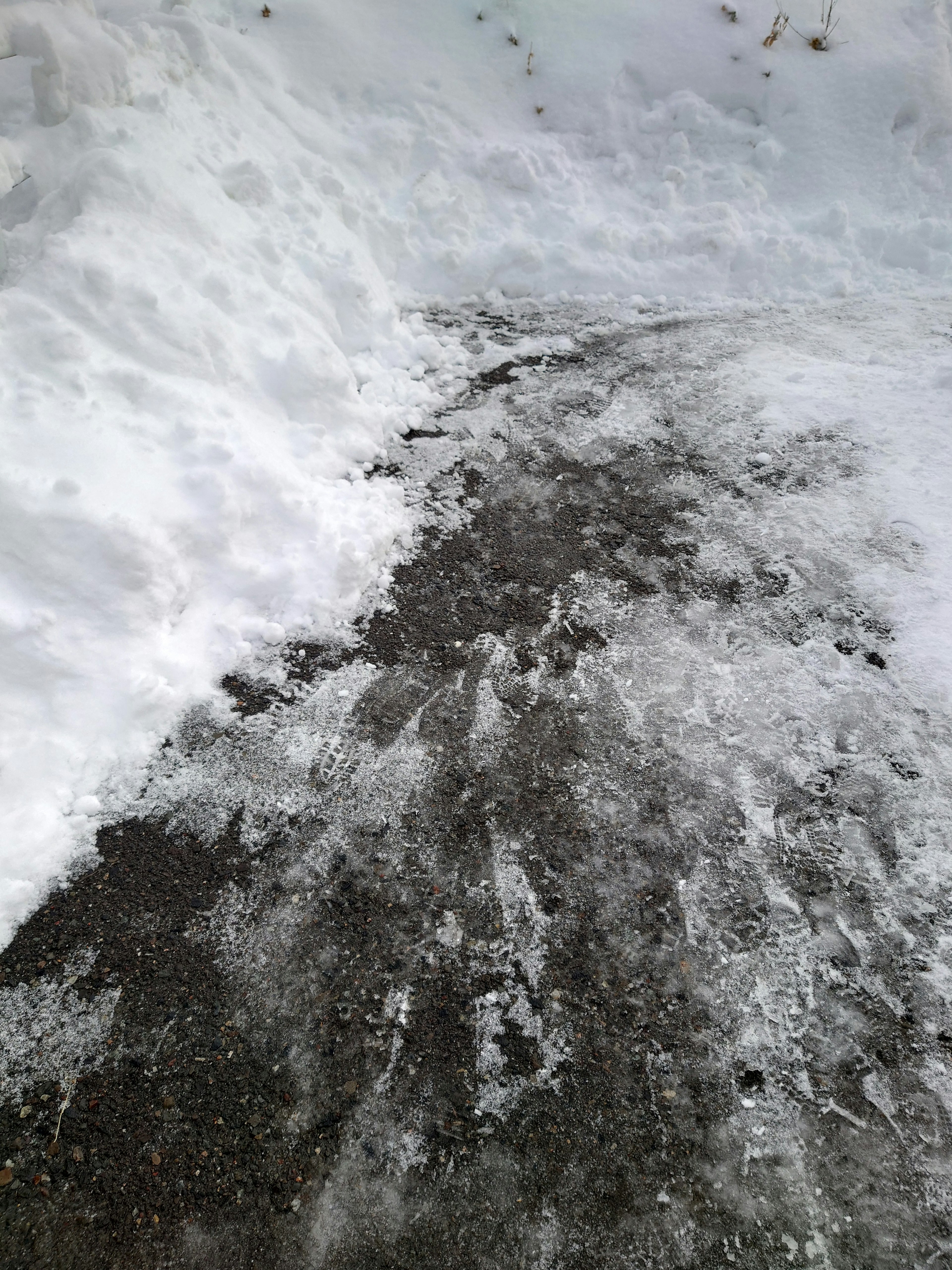 Un chemin partiellement dégagé de neige avec des plaques de glace visibles