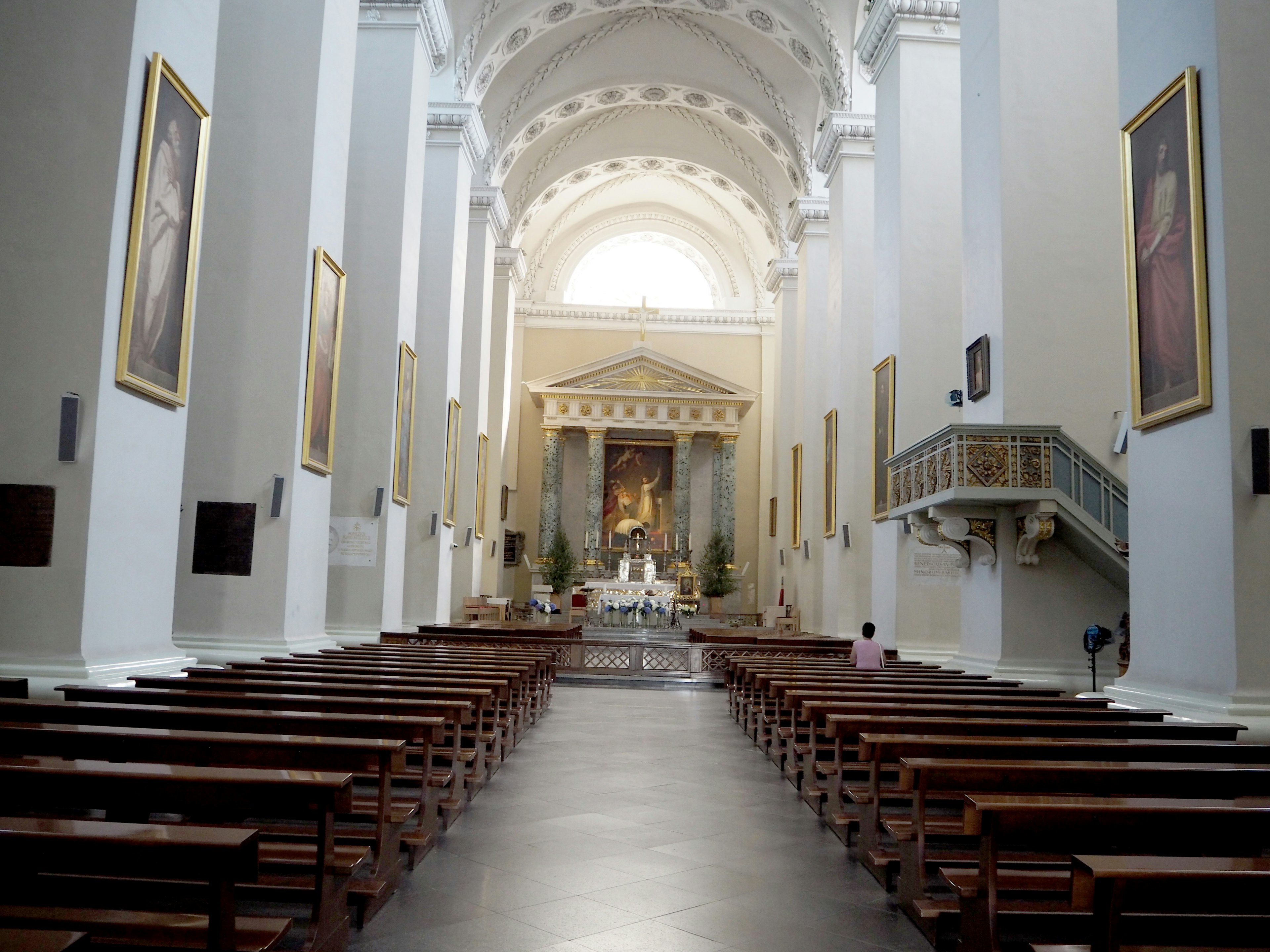 Interior of a spacious church featuring long pews and a high ceiling with vibrant paintings on the walls