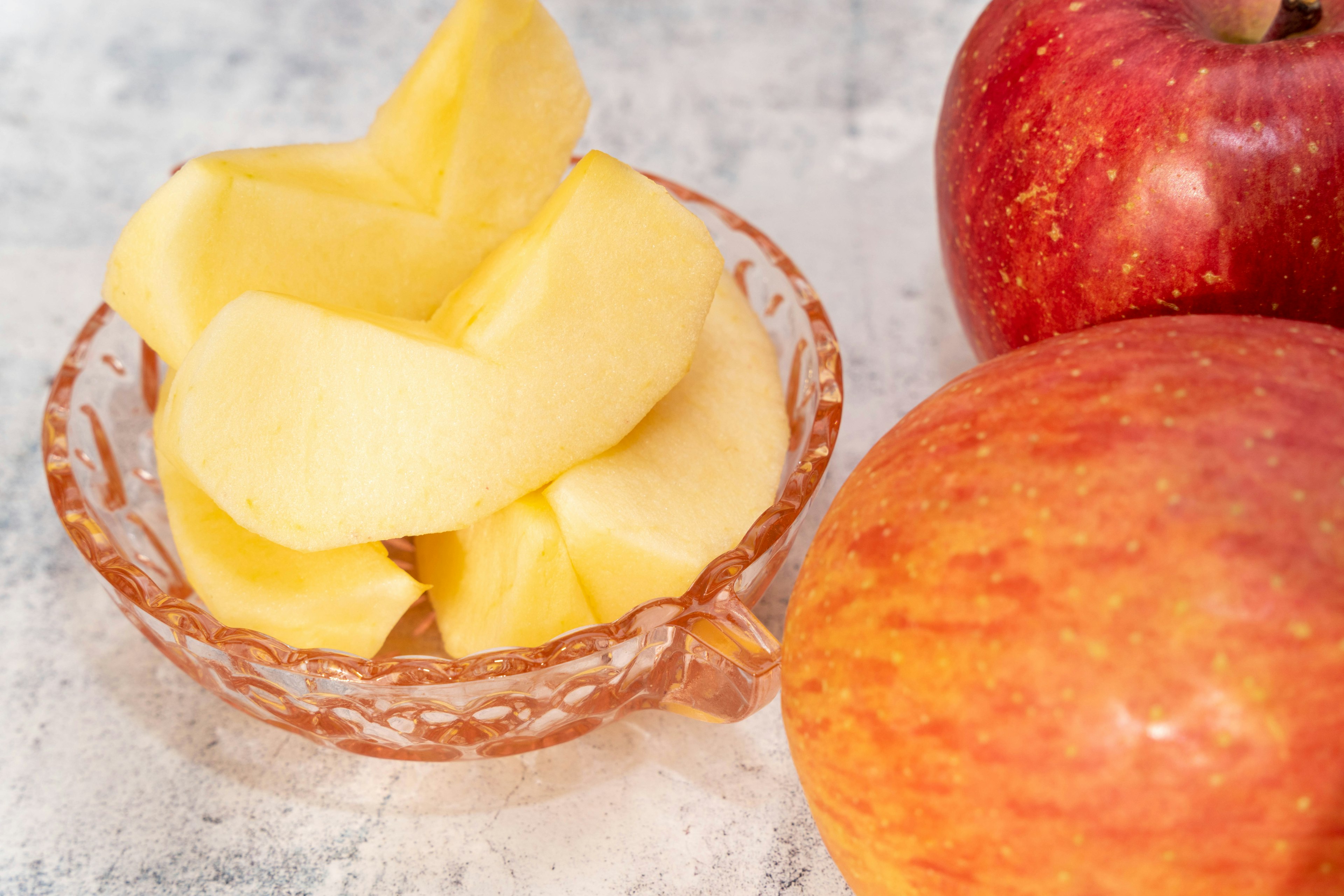 Red apple and slices of yellow apple in a glass bowl