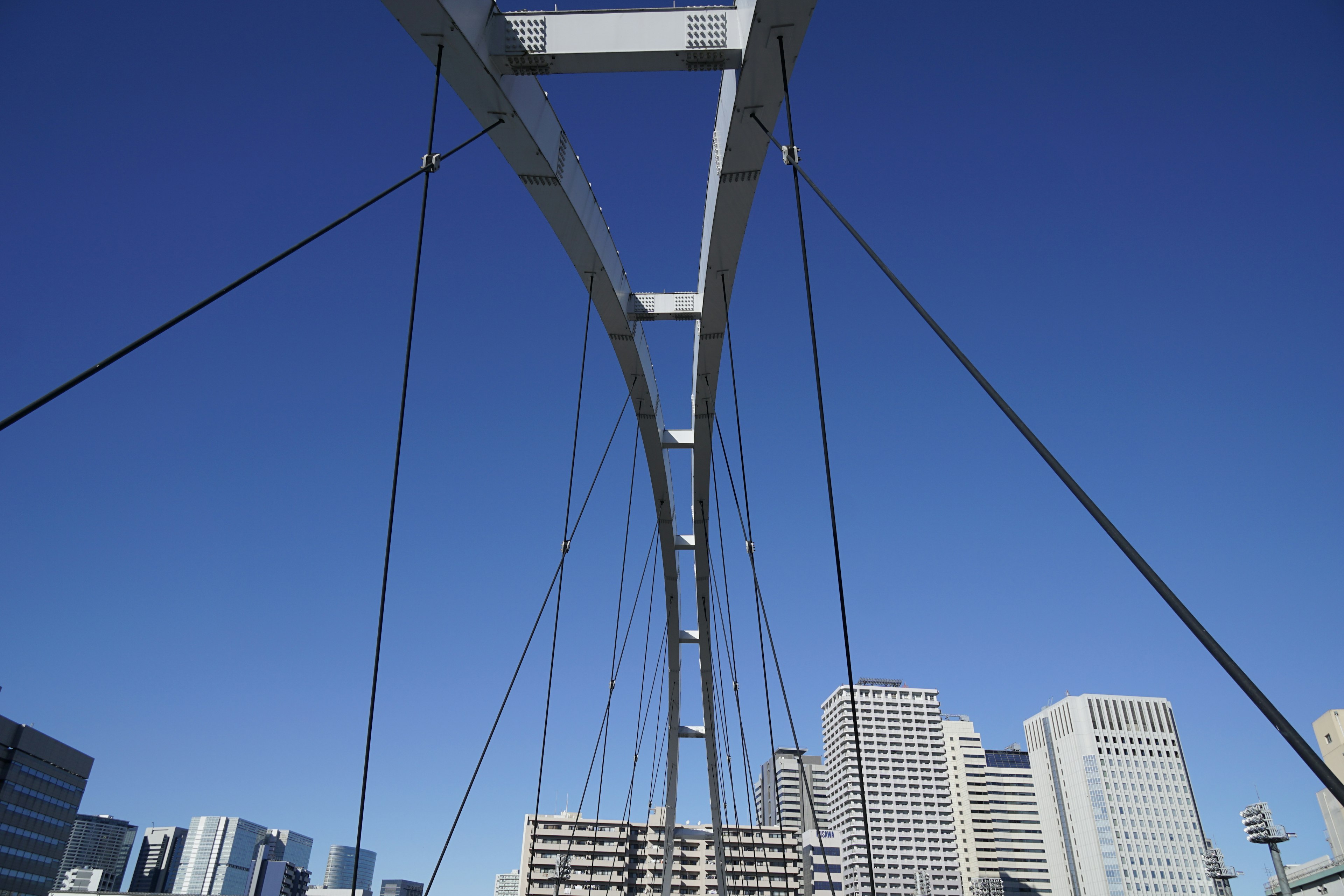 Struttura di ponte sospeso sotto un cielo blu con grattacieli circostanti