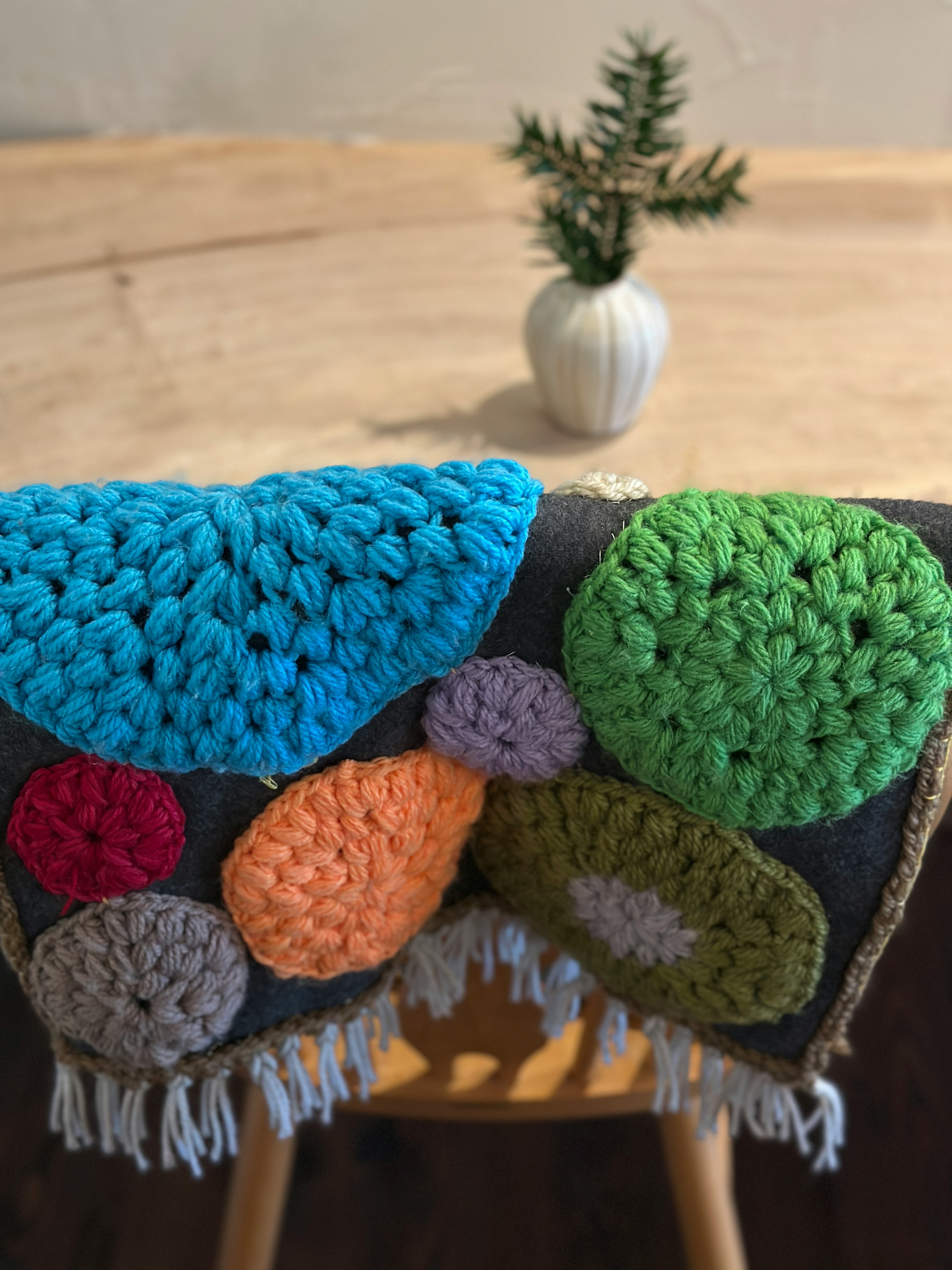 Colorful crocheted blanket draped over a chair with a small plant in a white vase