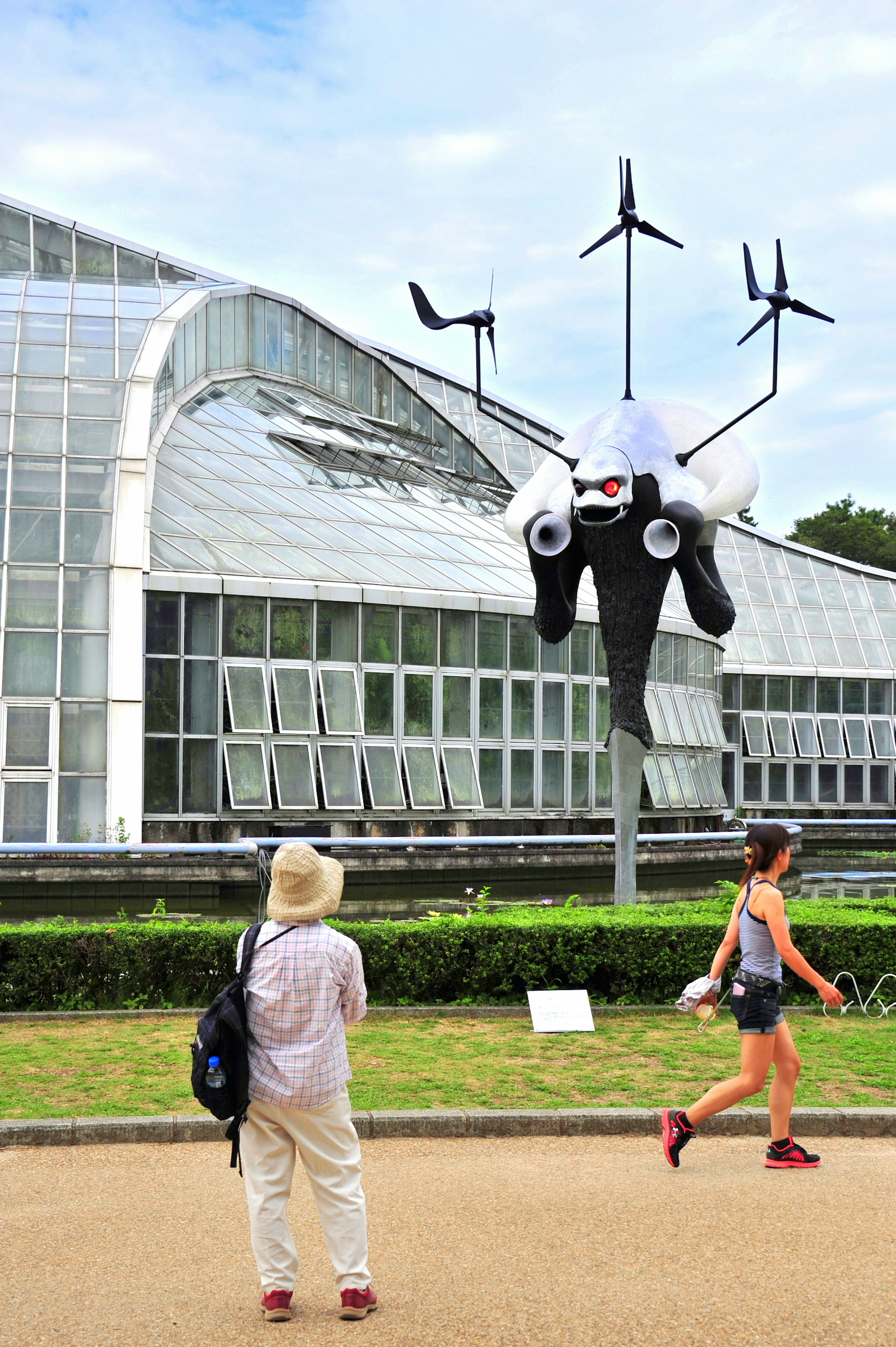 Una instalación artística gigante con turbinas eólicas frente a un invernadero con visitantes