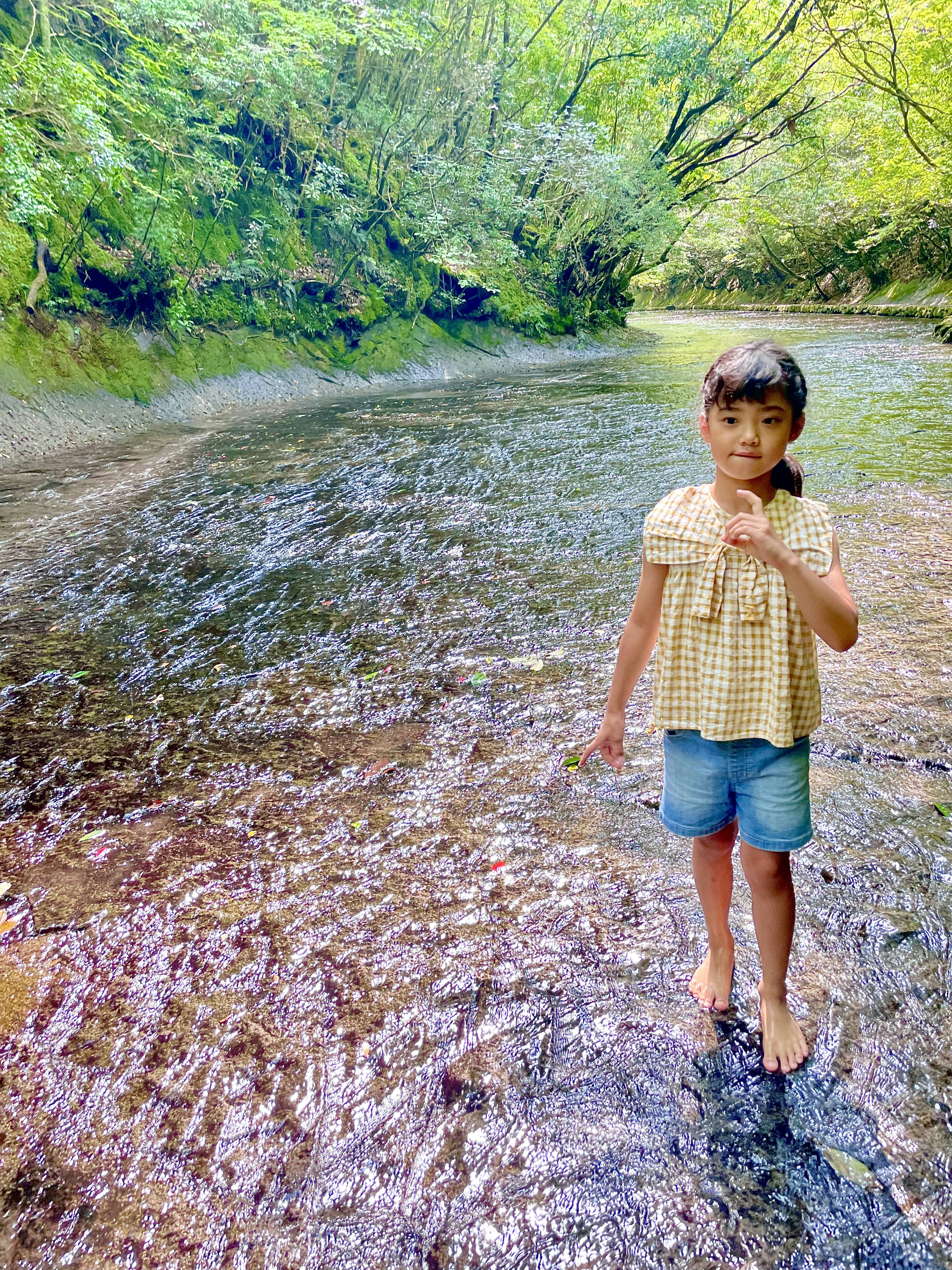 Seorang gadis berdiri di sungai dikelilingi oleh pepohonan