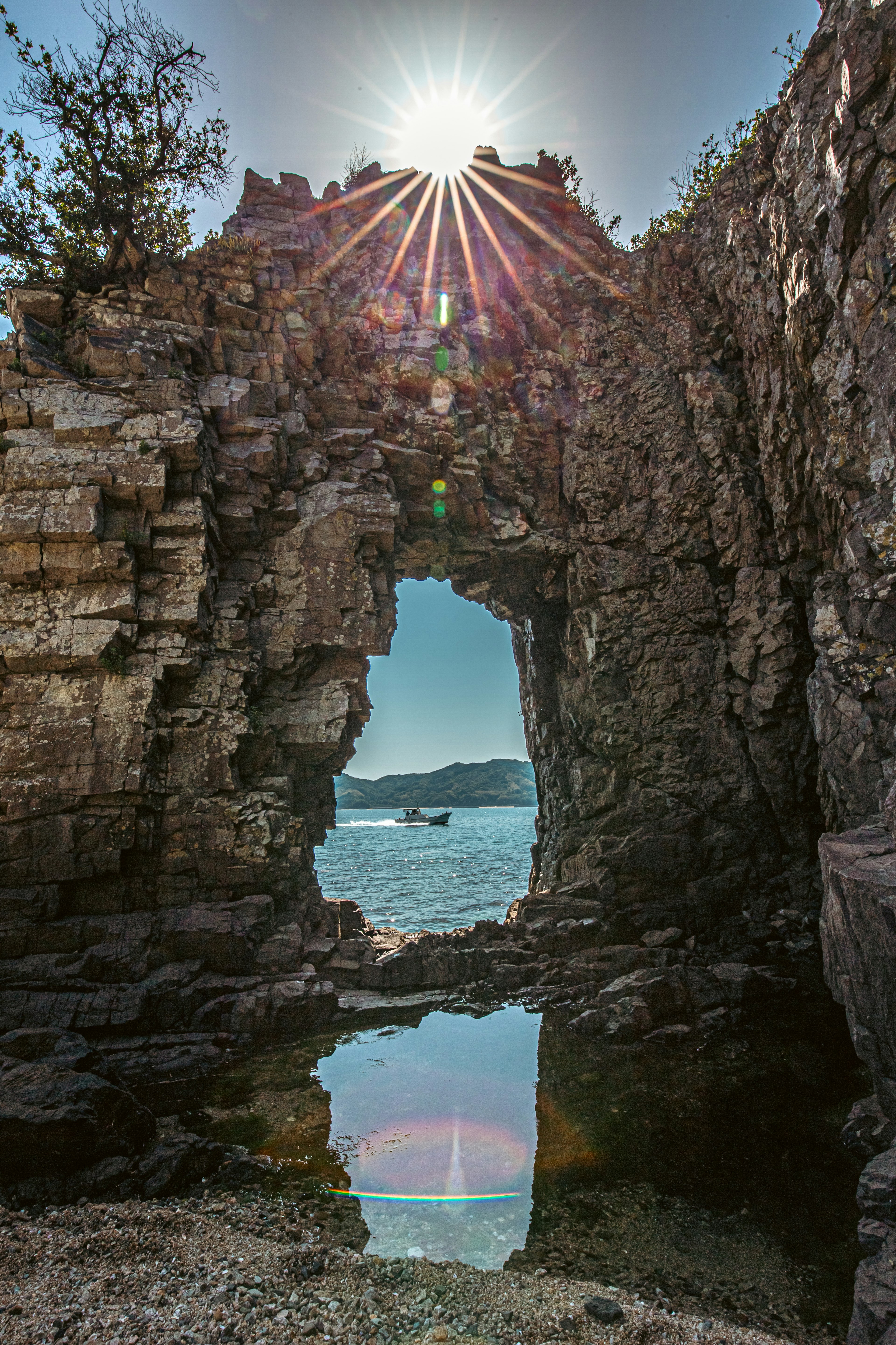 Luz del sol brillando a través de un arco de roca con vista al mar