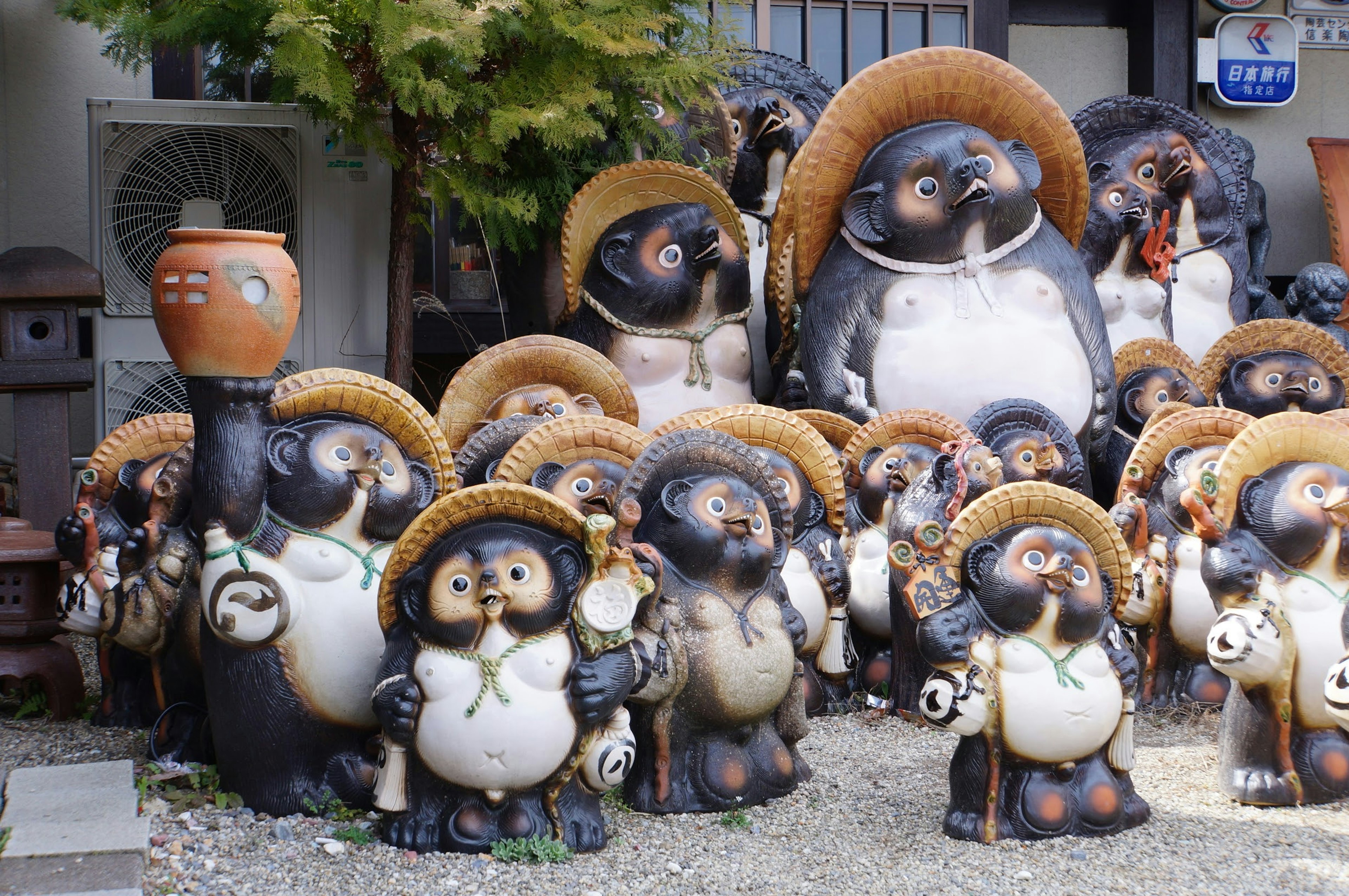 A collection of ceramic tanuki figures wearing straw hats displayed outdoors