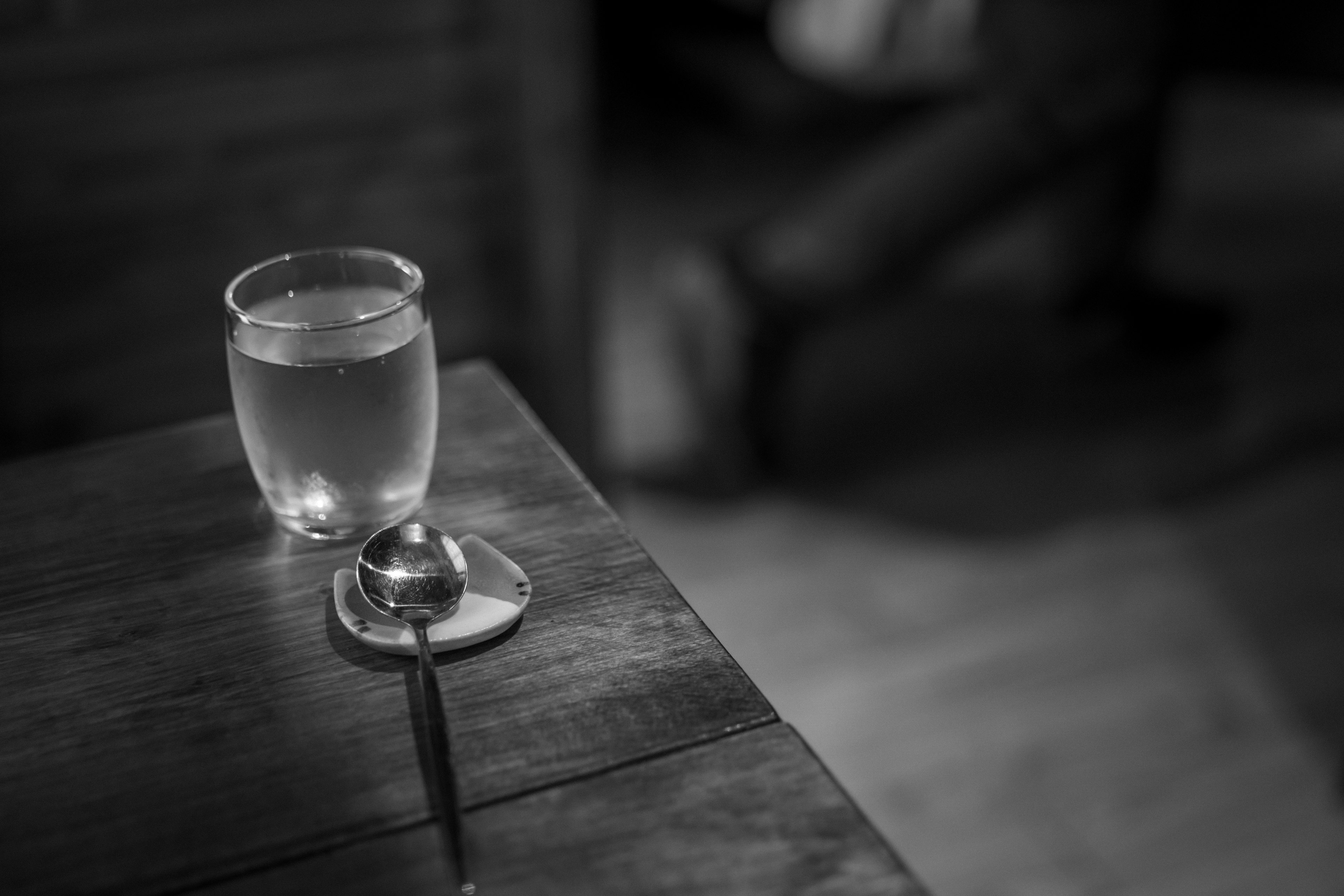 A glass of clear drink on a wooden table with a spoon