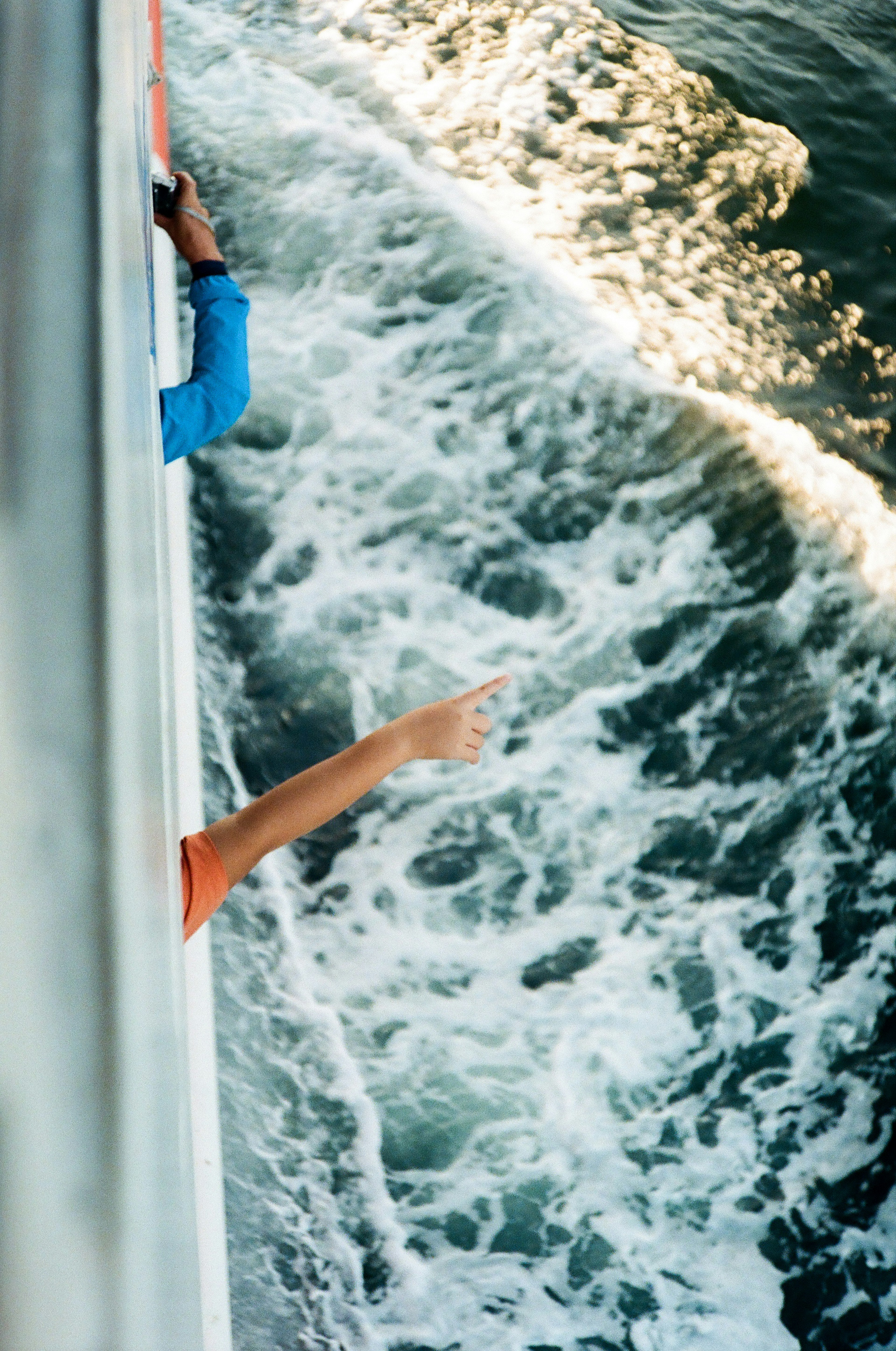 View of hands pointing over the side of a boat with ocean waves