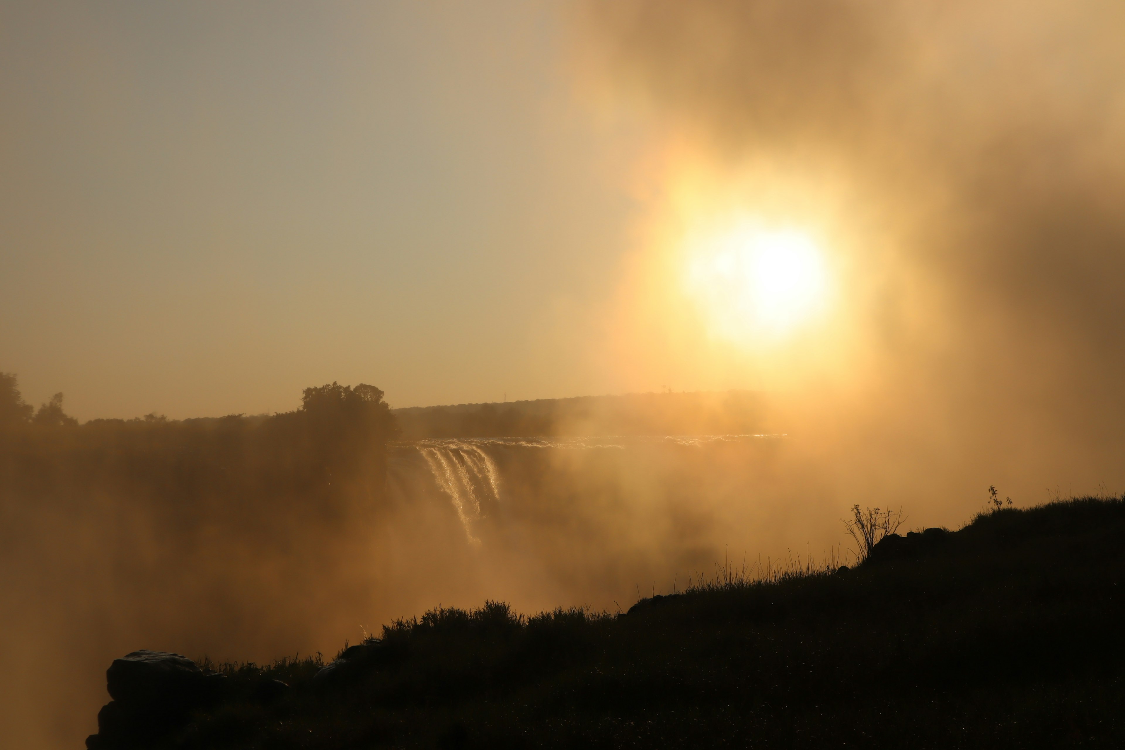 Silueta de una cascada y un atardecer envueltos en niebla