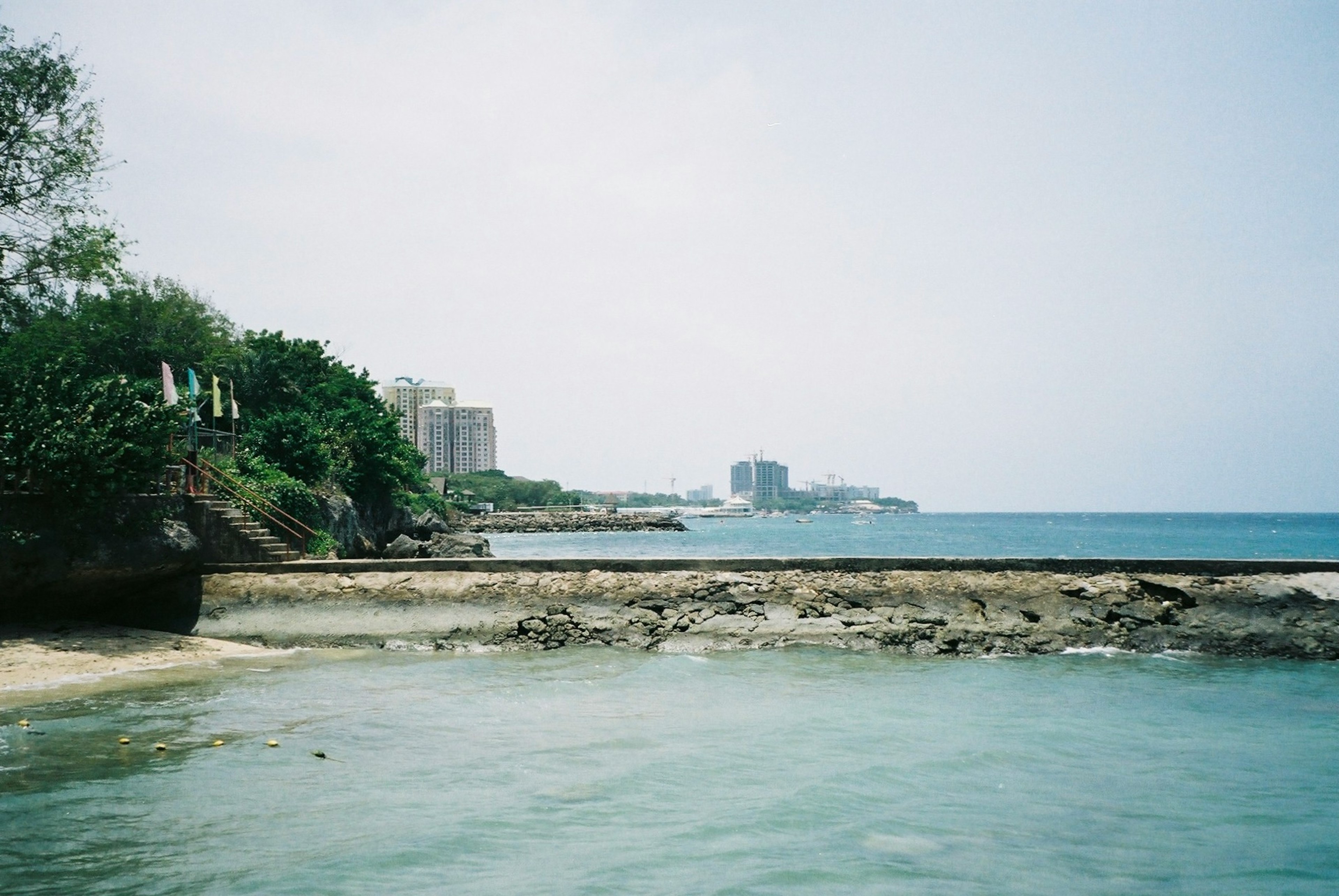 海岸に沿った風景で、遠くにビルが見える穏やかな海