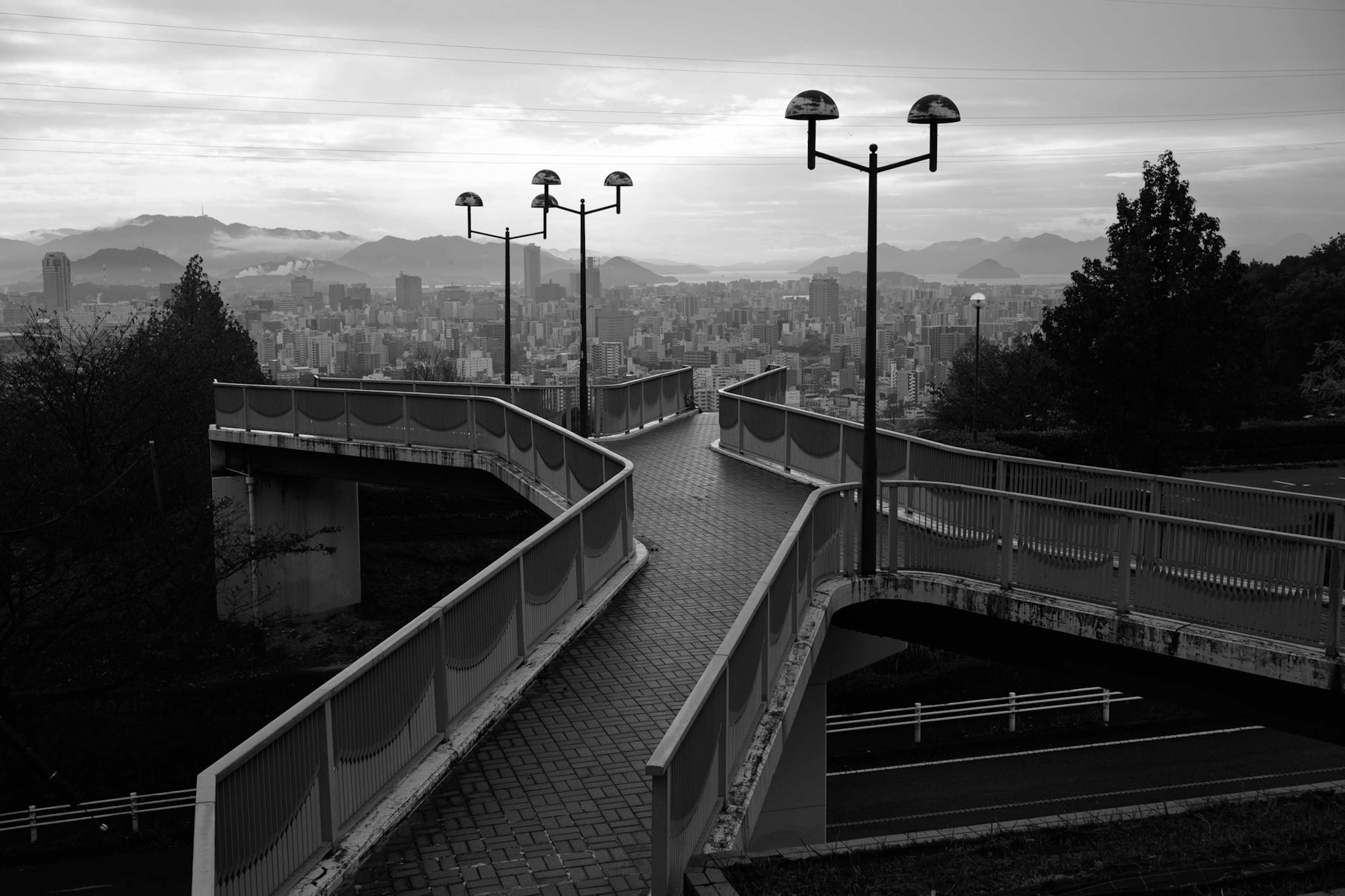 Curved walkway in black and white with street lamps and distant hills