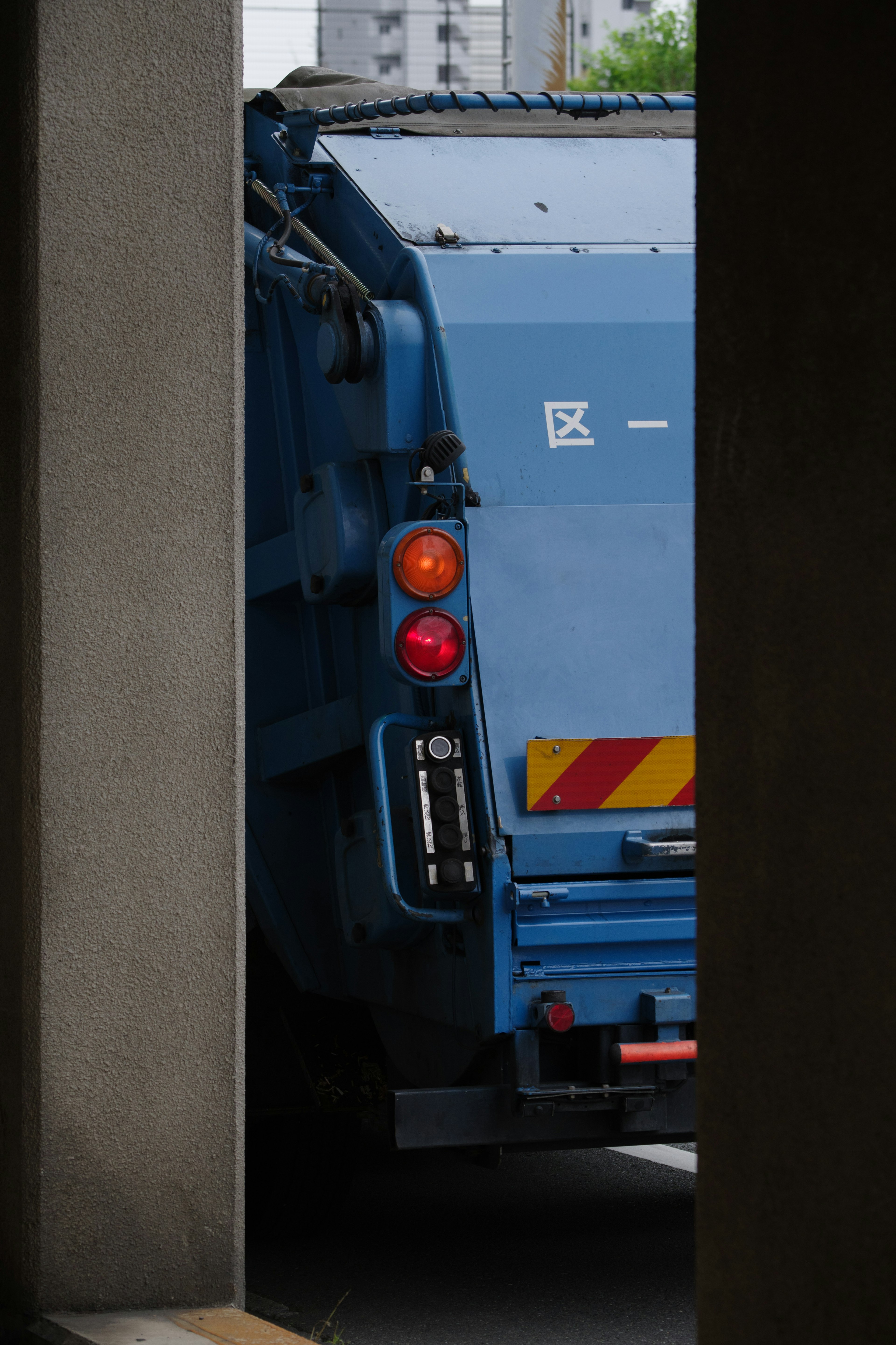 Blue garbage truck visible between buildings