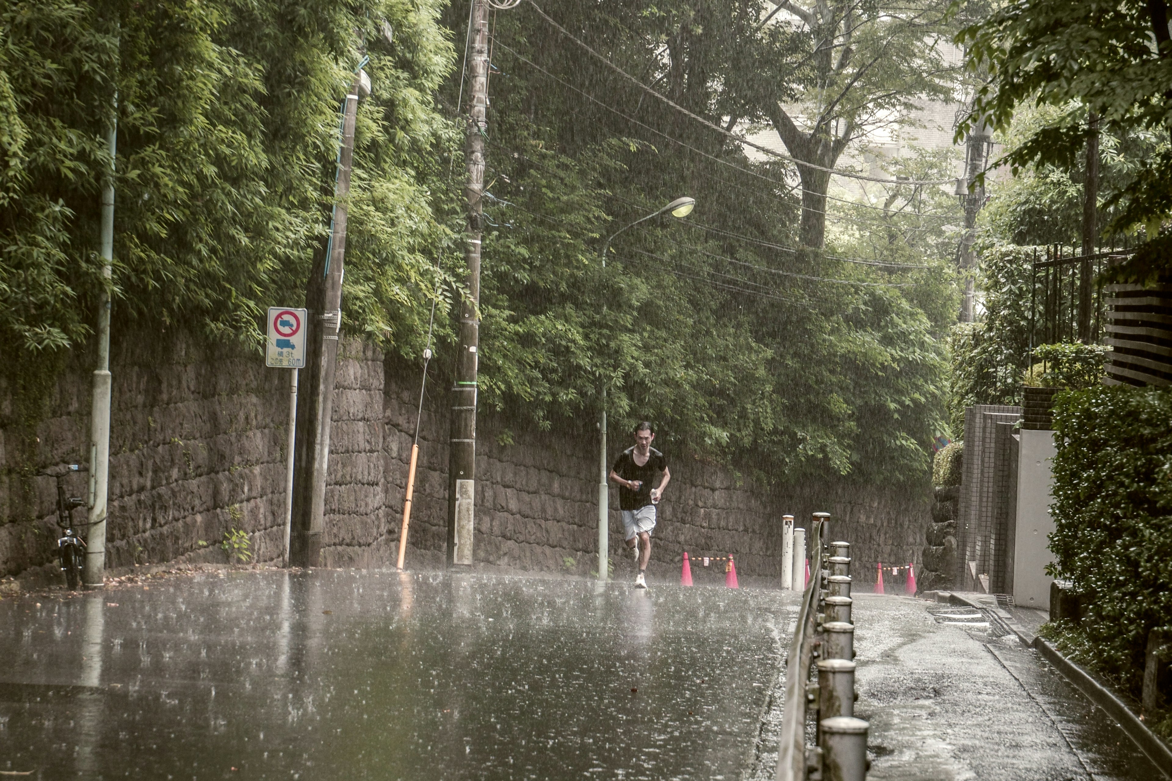 A man running in the rain on a quiet street surrounded by lush greenery