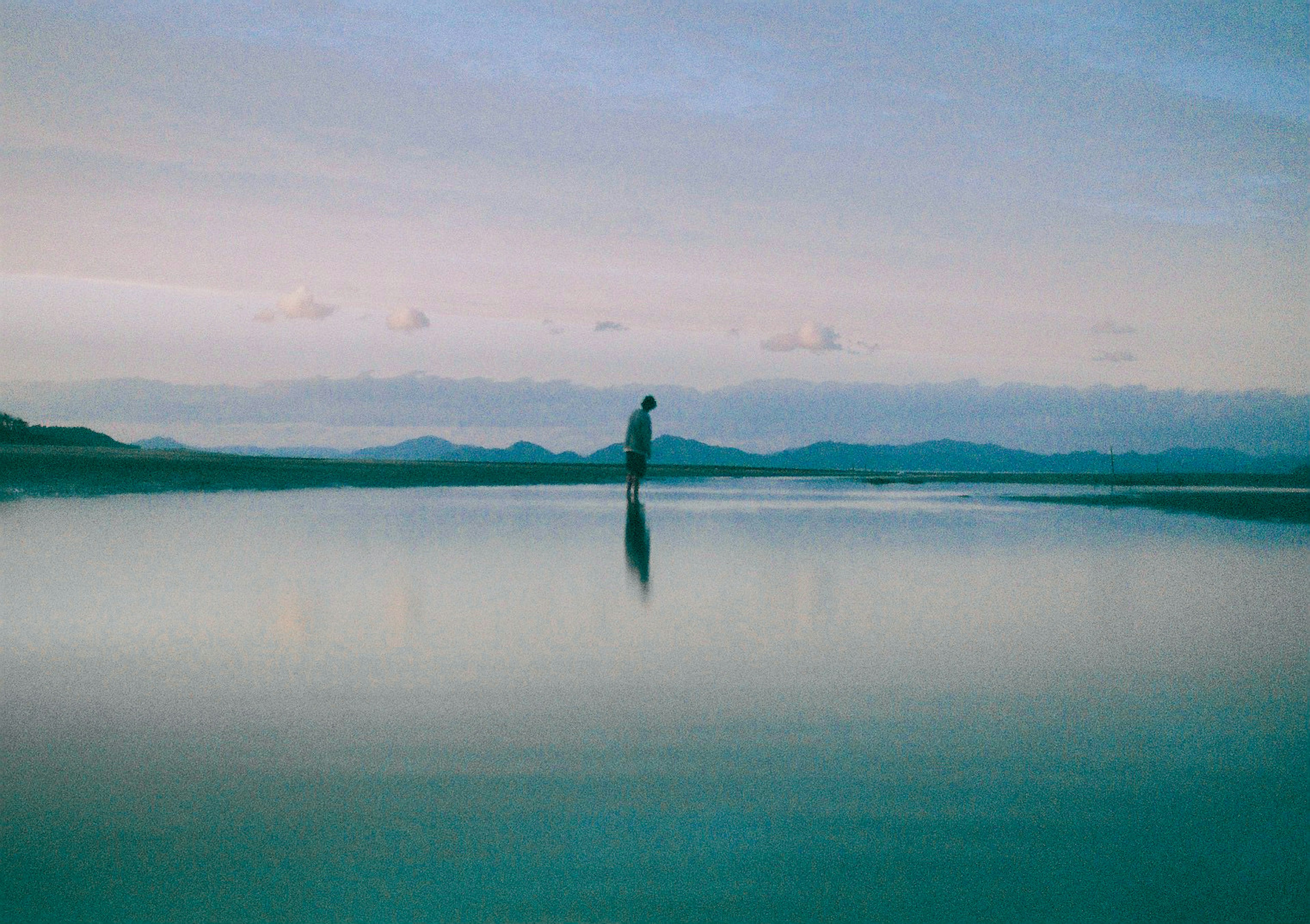 A silhouette of a person standing on a calm water surface with reflections