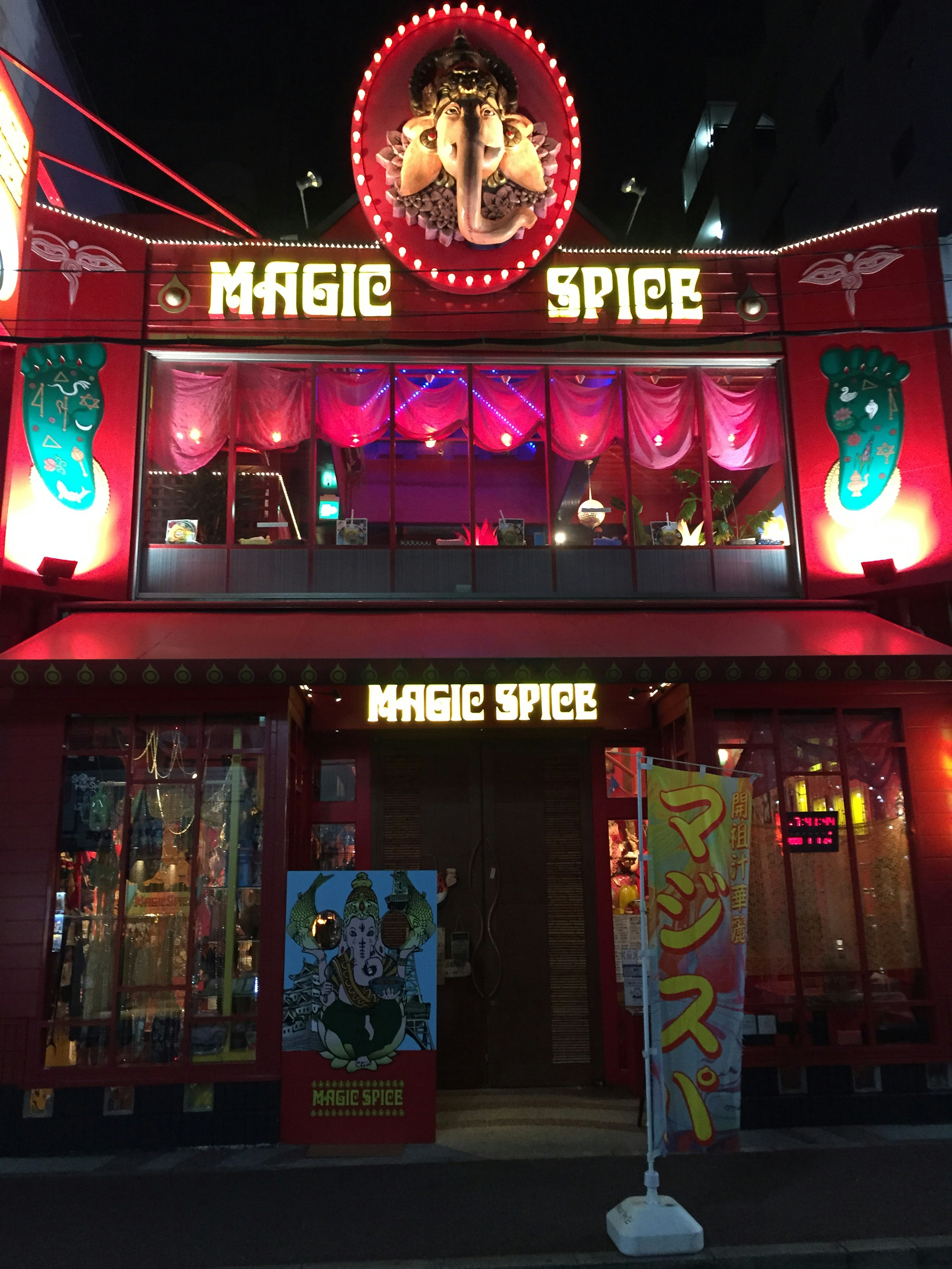 Exterior of Magic Spice restaurant illuminated at night with vibrant red and blue neon lights