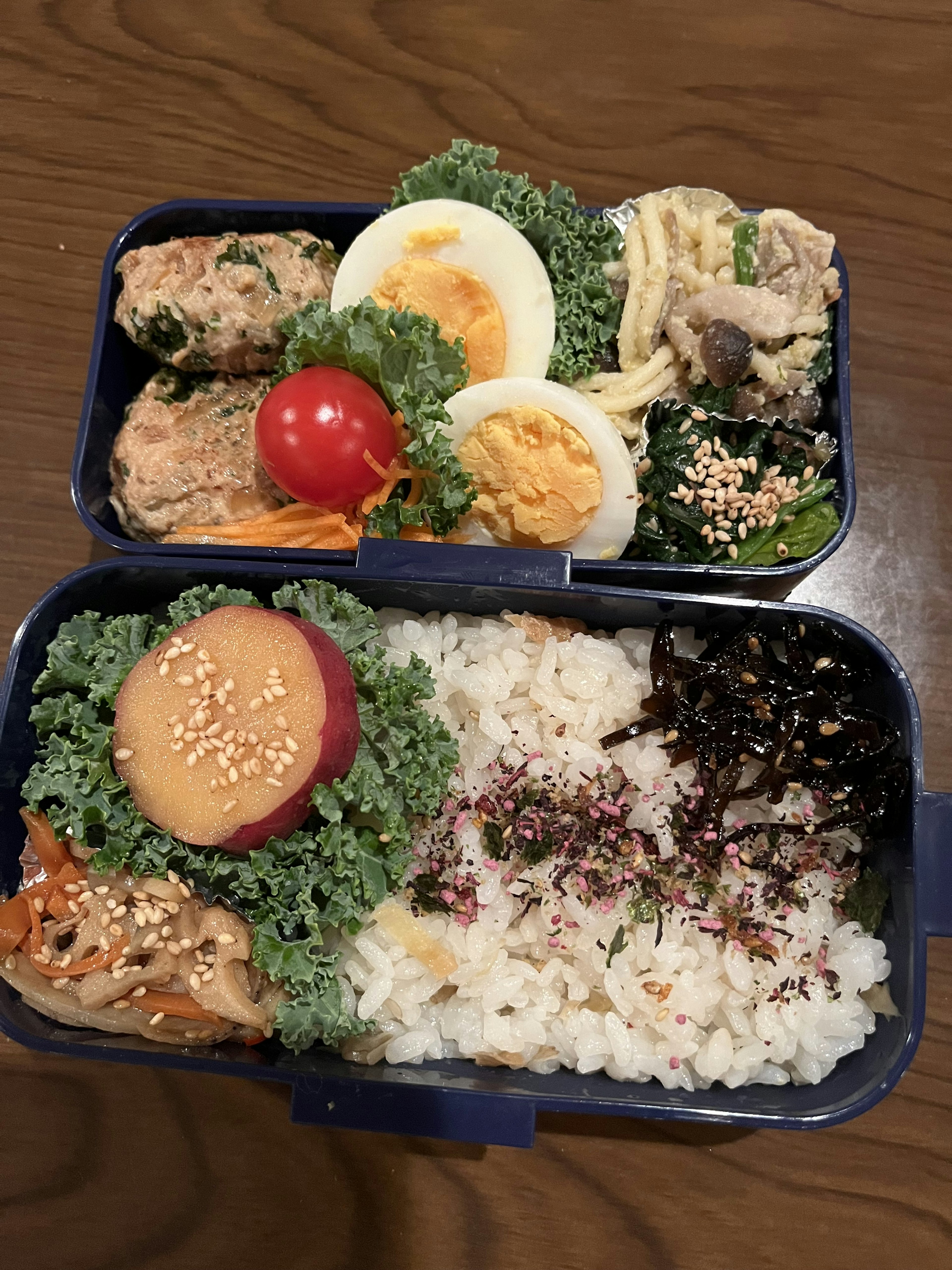 Zwei-stufige Bento-Box mit Eiern, Tomate und Gemüse im oberen Fach und Reis mit Beilagen im unteren Fach