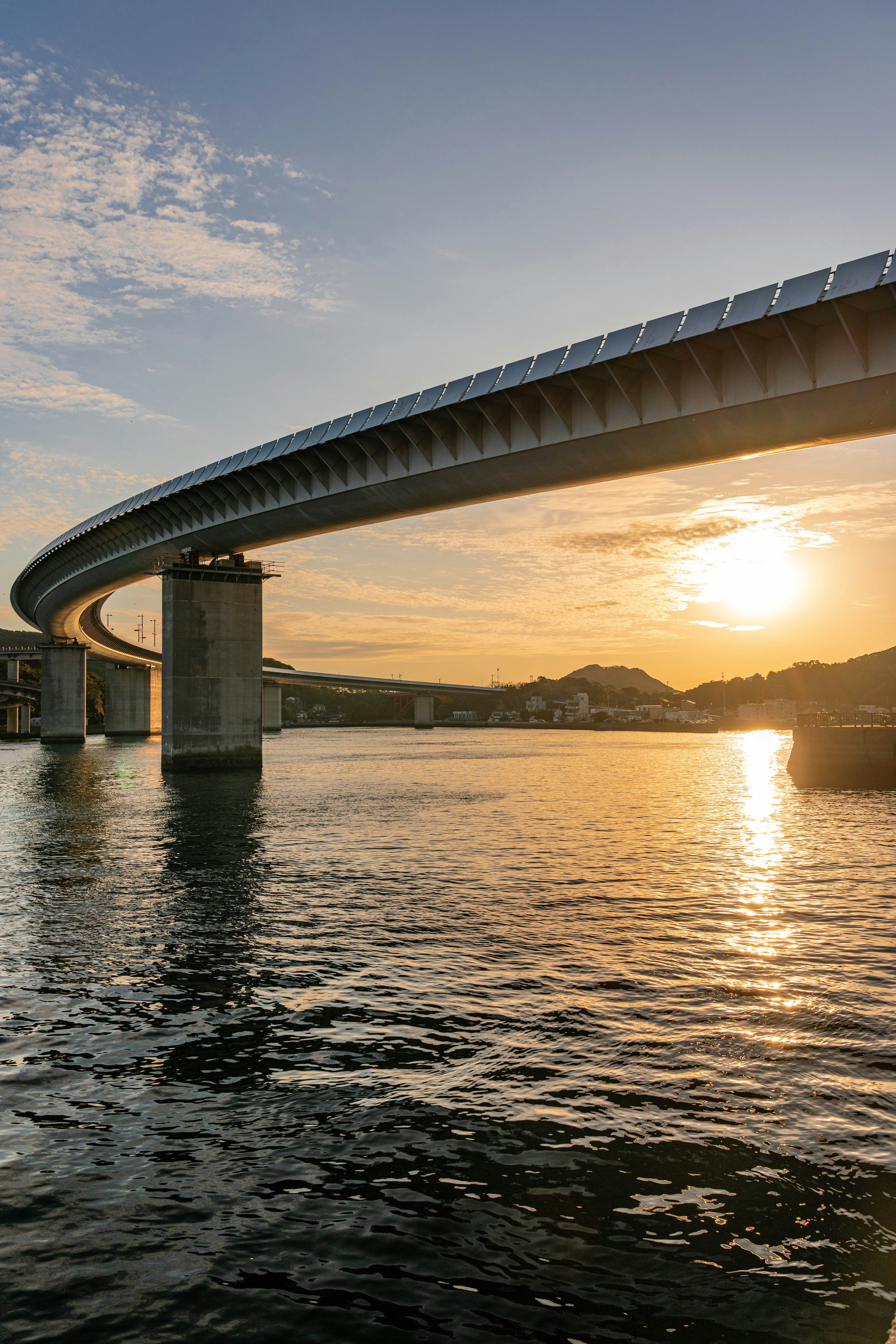 Futuristic bridge arching over water with sunset reflections