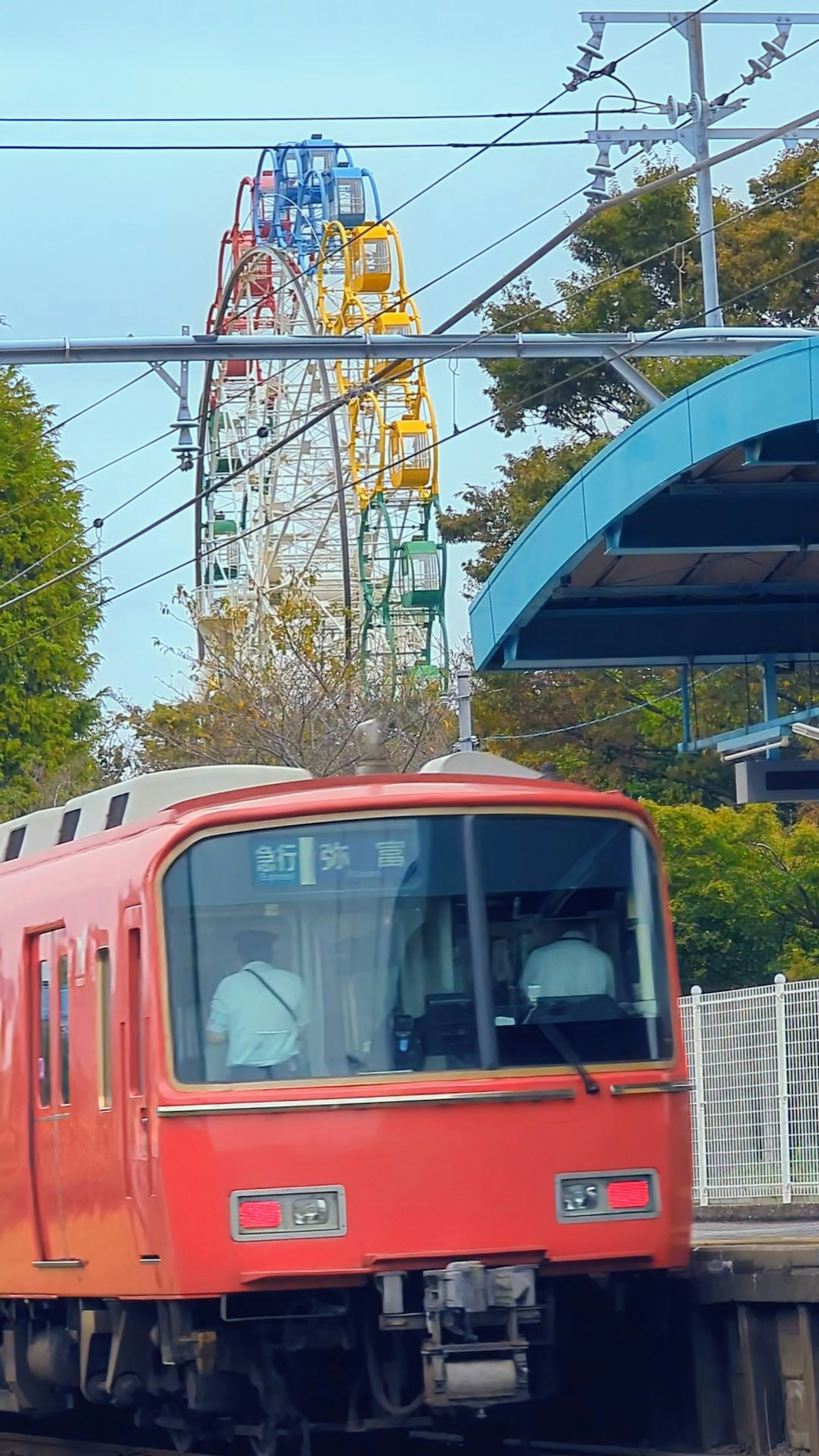 Kereta merah berhenti di stasiun dengan bianglala di latar belakang