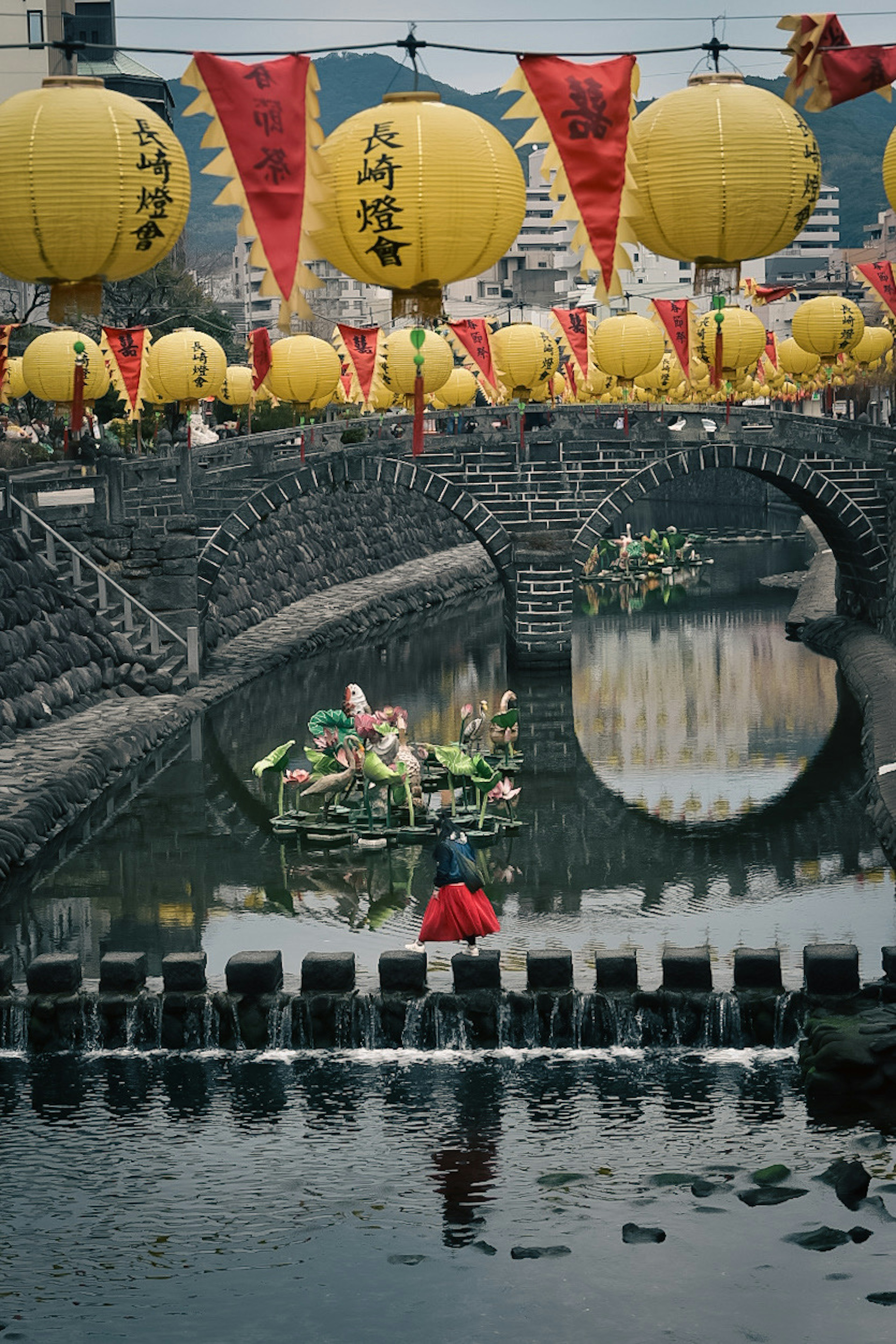 Una vista panoramica di lanterne colorate e bandiere sopra un ponte di pietra con persone in barca su un fiume tranquillo