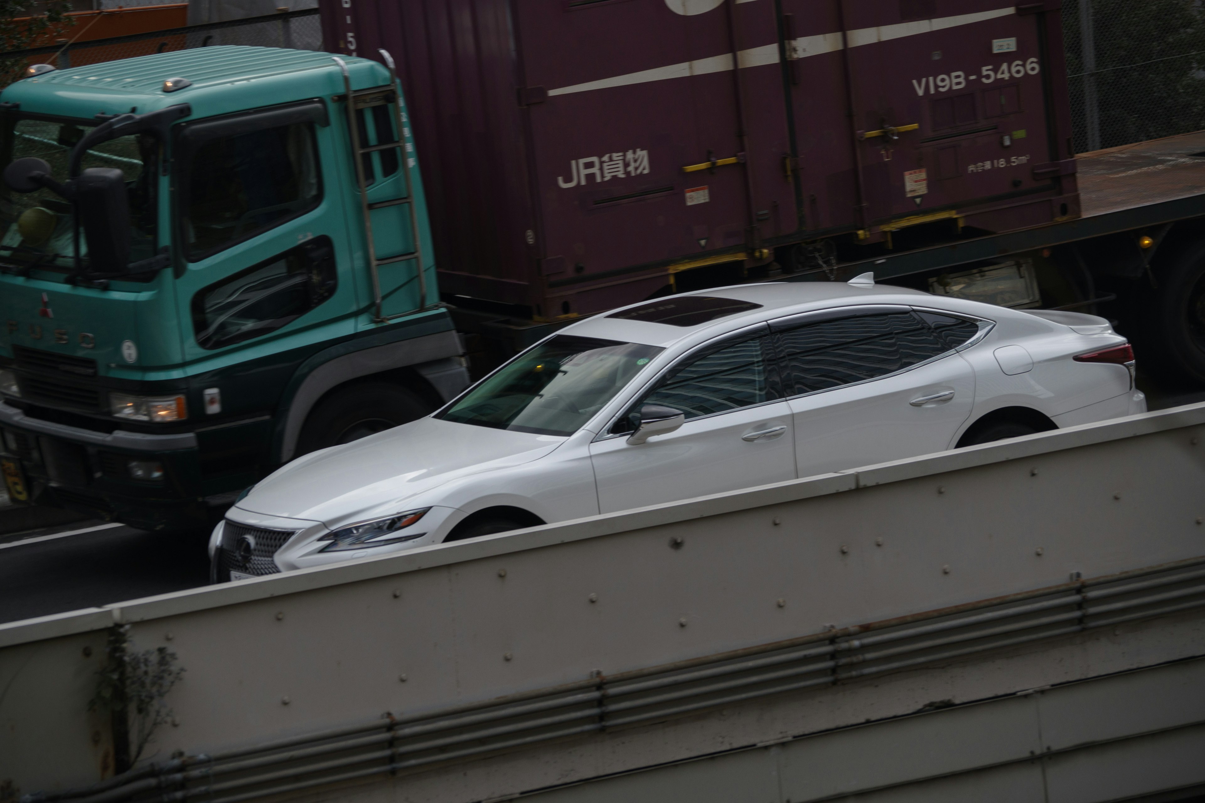 白い自動車と緑のトラックが並走する都市の道路の風景