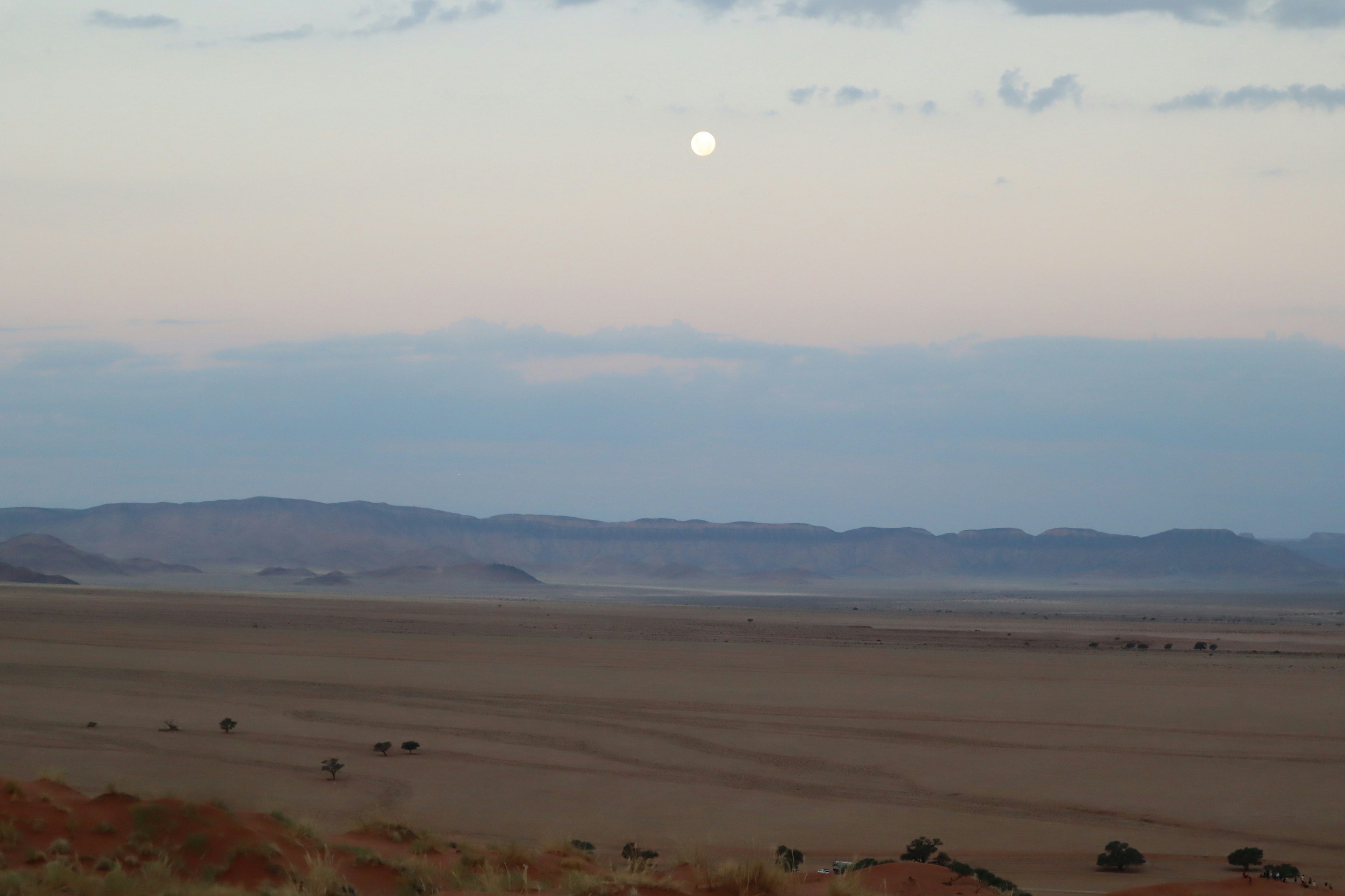 Vast desert landscape with a glowing moon and soft blue sky