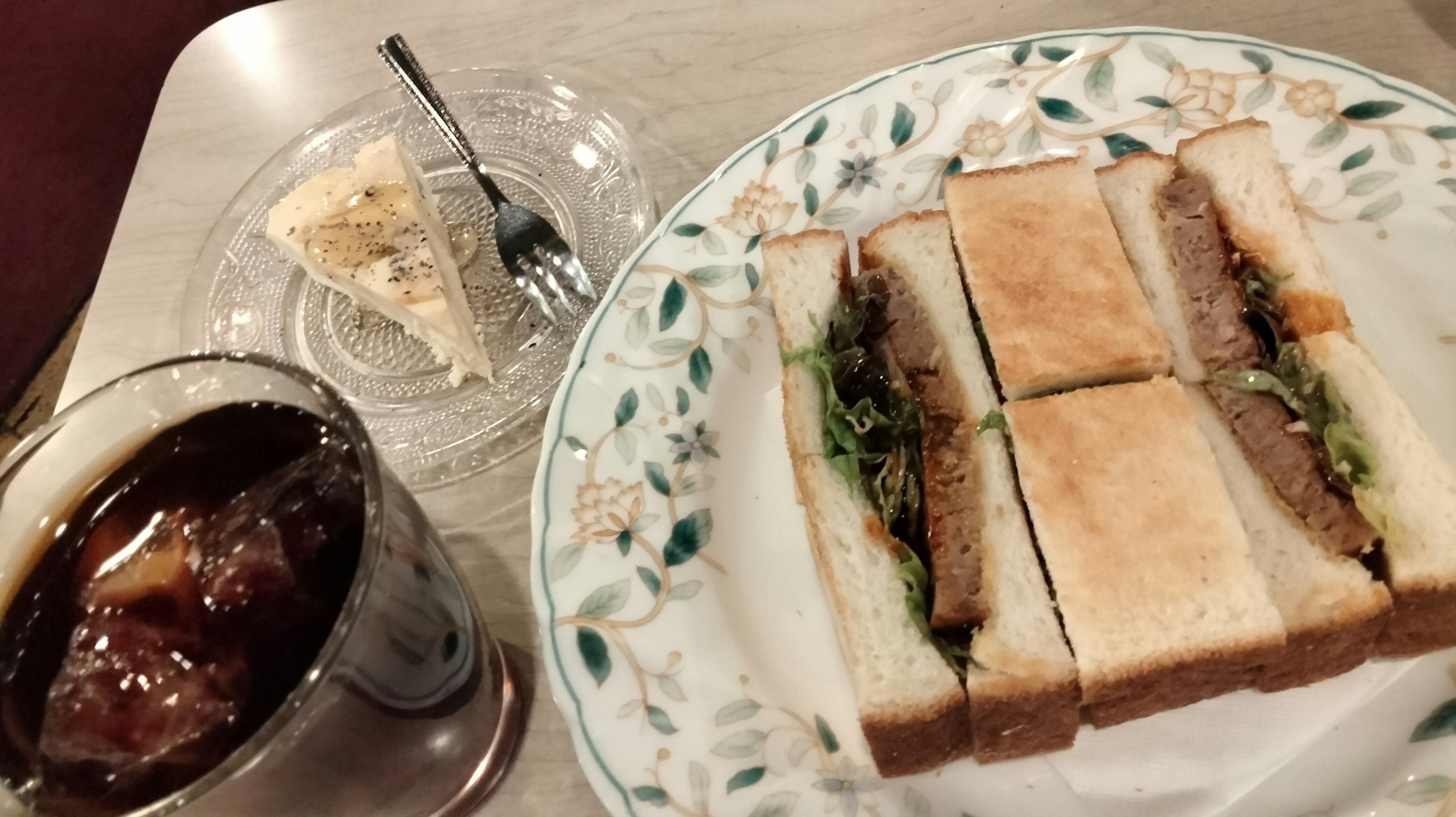 A plate featuring sandwiches with lettuce and meat alongside iced coffee and a dessert slice