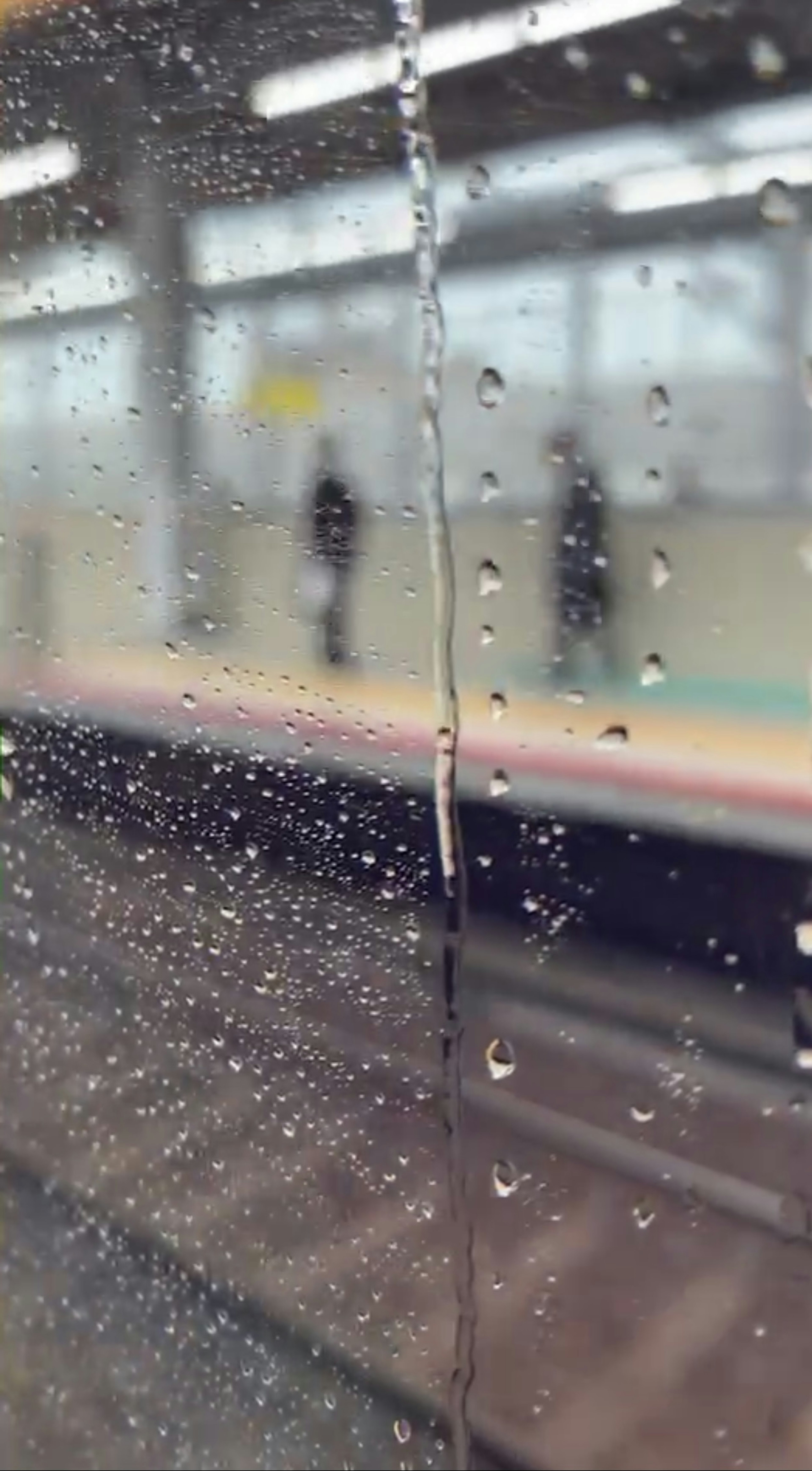 雨滴のついた窓越しに見える駅のプラットフォームと人影