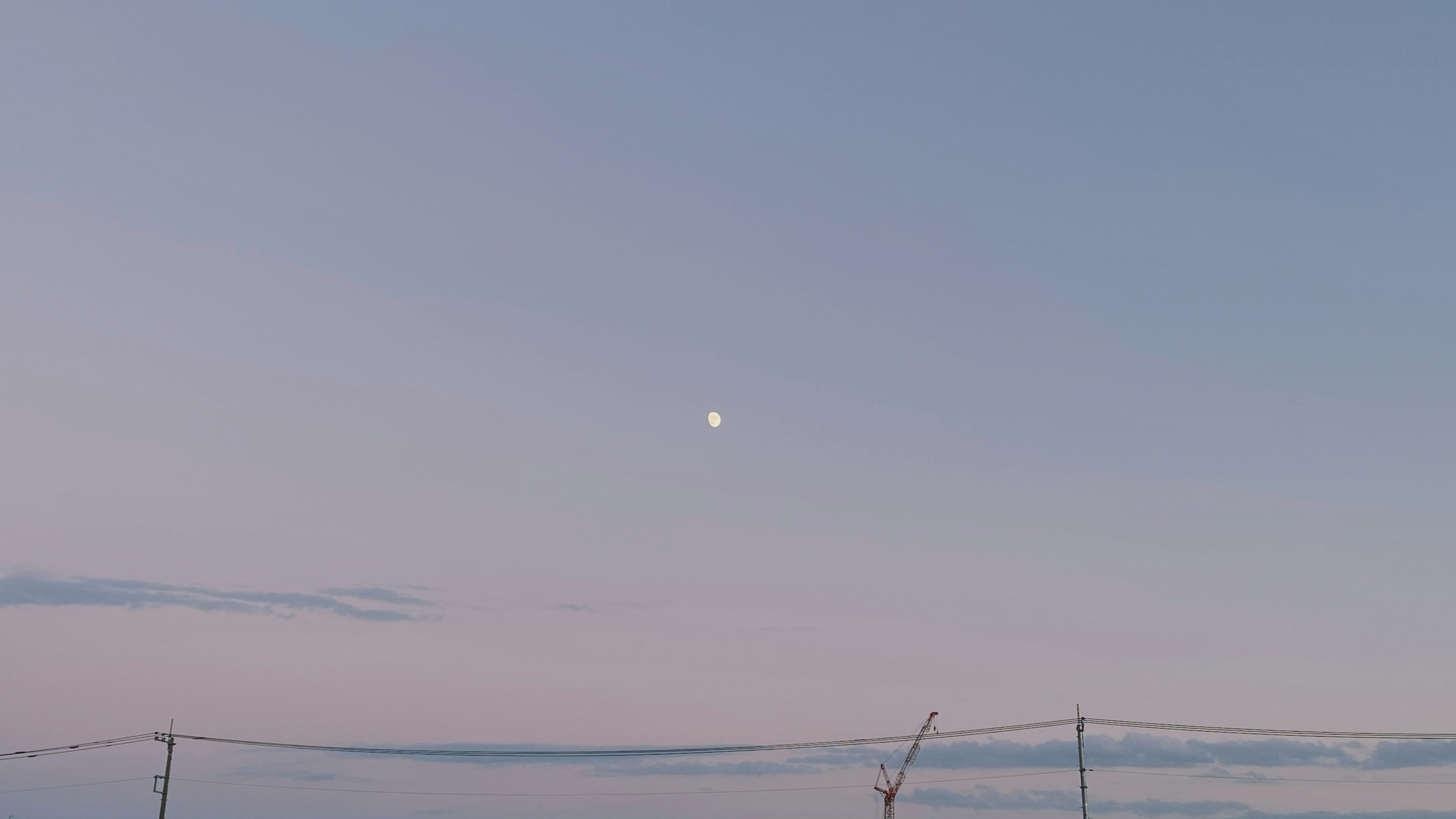 Una luna pálida visible en un cielo azul durante el crepúsculo