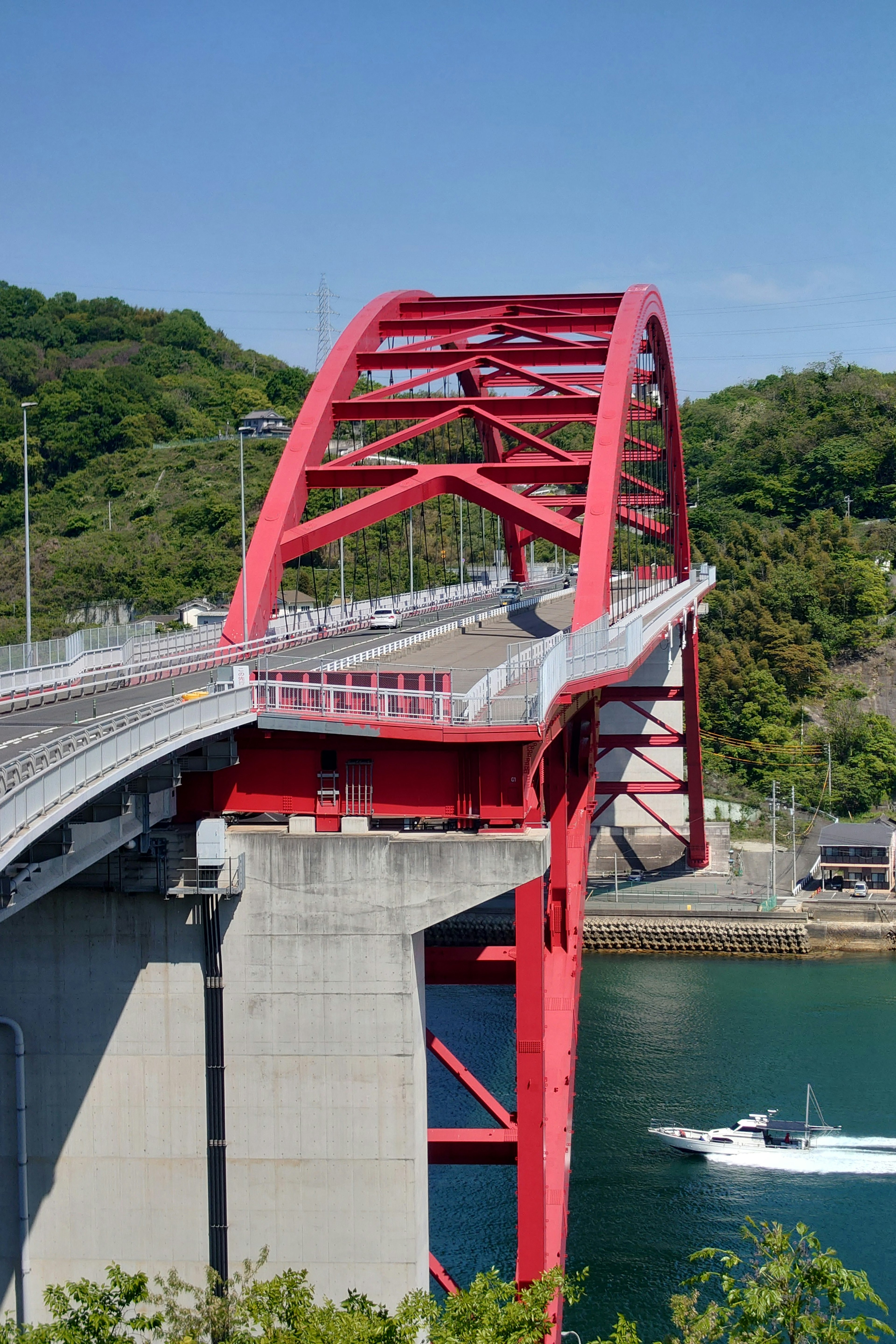 สะพานโค้งสีแดงพร้อมทิวทัศน์สีเขียวและน้ำสีน้ำเงิน