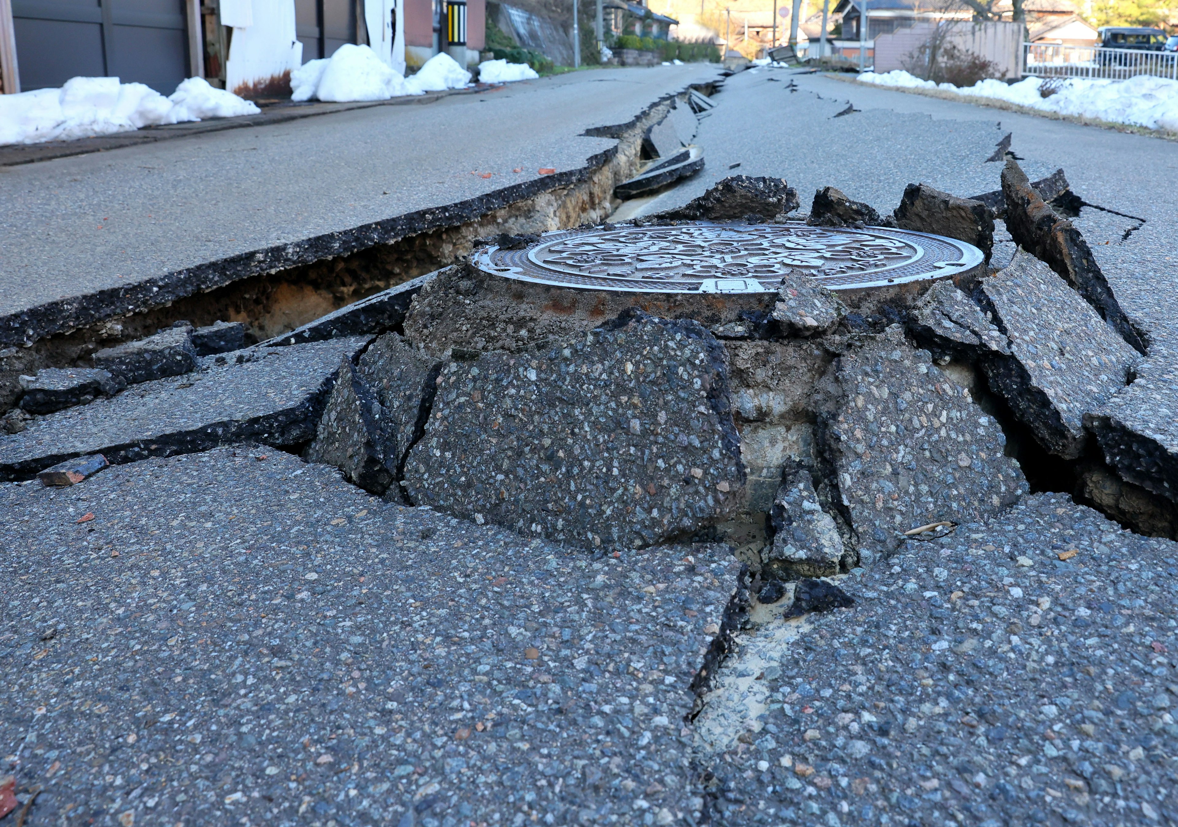 Rissige Asphaltstraße mit einem angehobenen Kanaldeckel