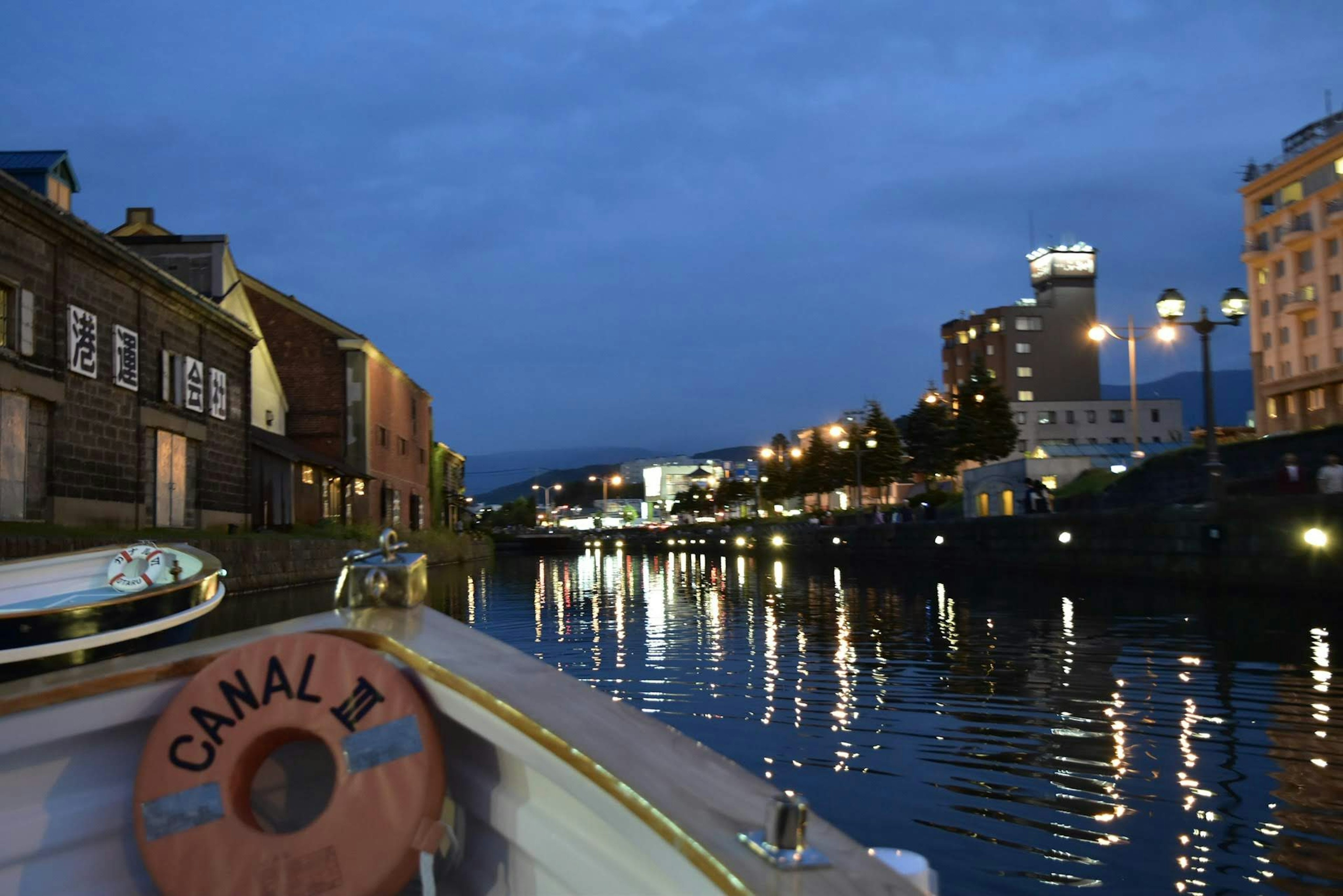 Vue du soir le long du canal avec un bateau portant l'inscription "CANAL" et des reflets sur l'eau