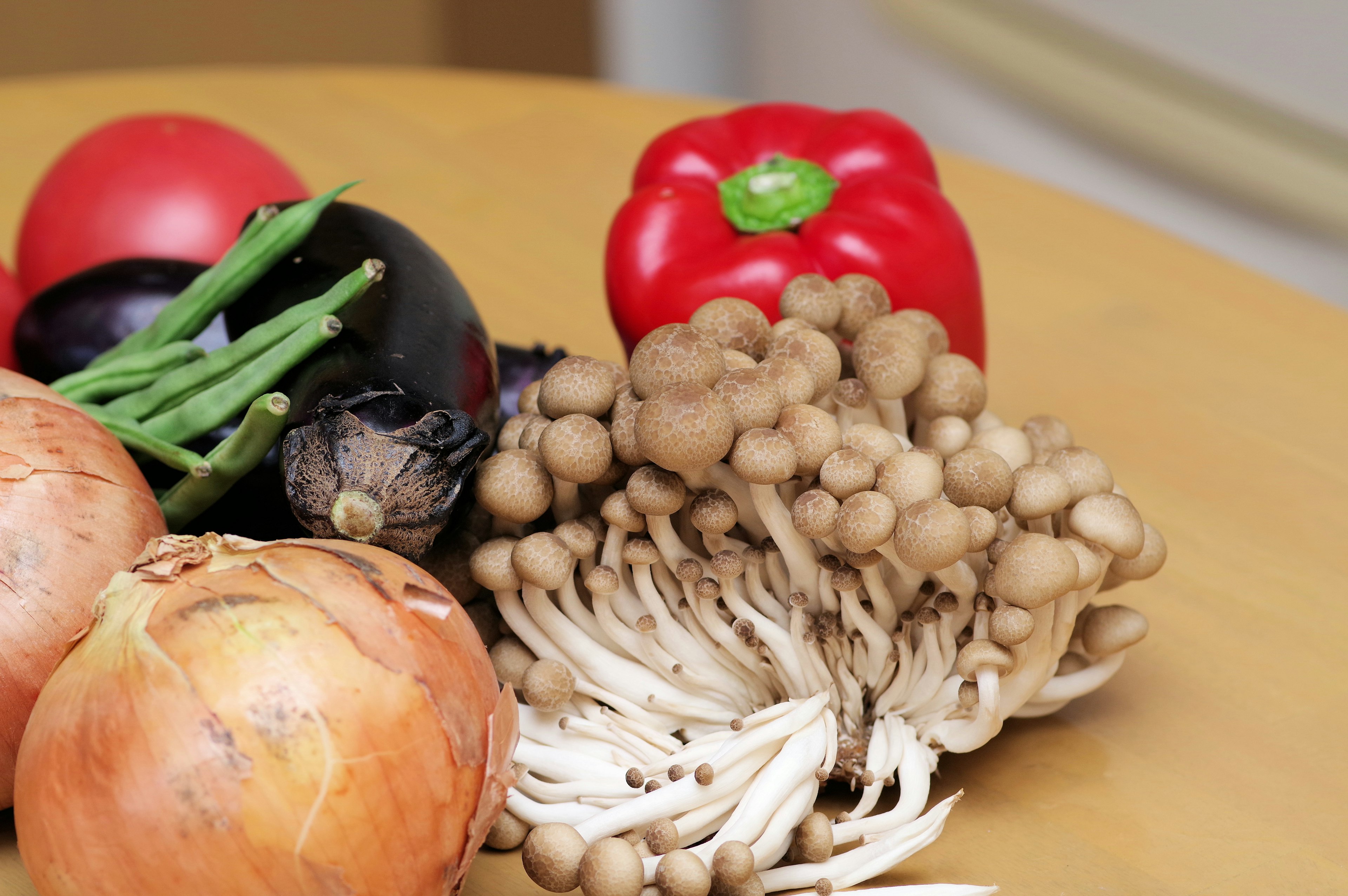 Fresh vegetables including red bell pepper mushrooms onions and tomatoes on a wooden table