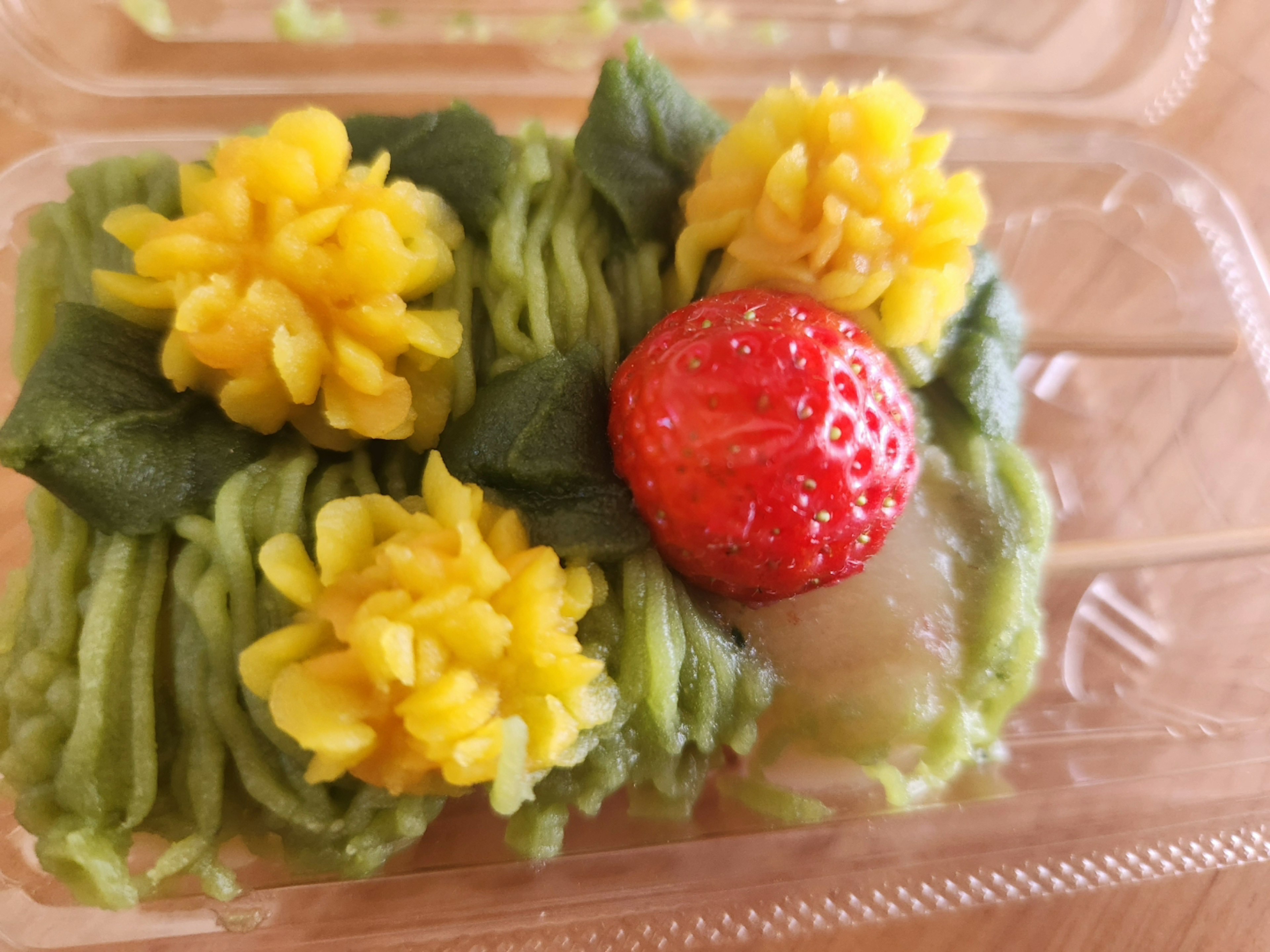 Postre con crema verde decorado con flores amarillas y una fresa roja