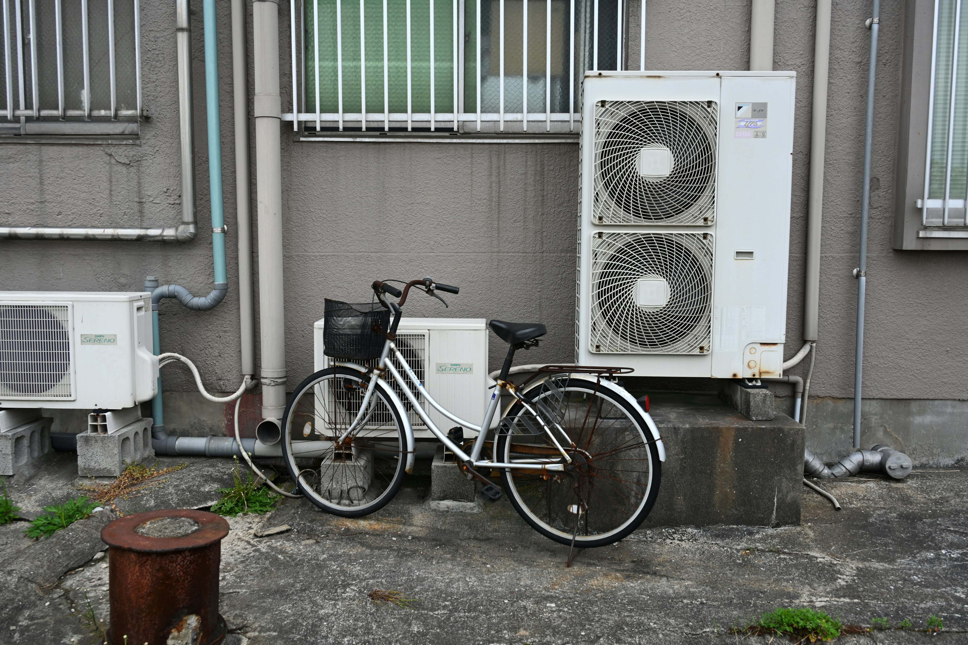 Weißes Fahrrad neben Klimaanlagen an der Außenwand eines Gebäudes